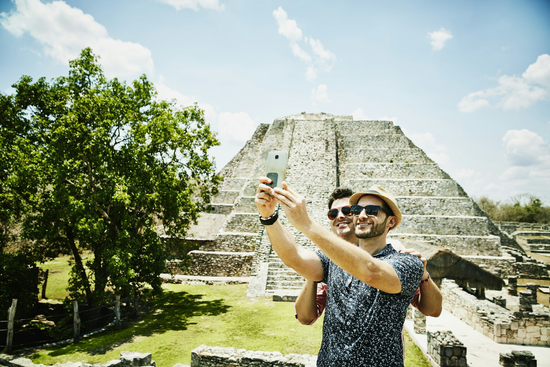 A couple posing for a selfie together in front of the Mayapan ruins in Mexico, on a gloriously sunny day.