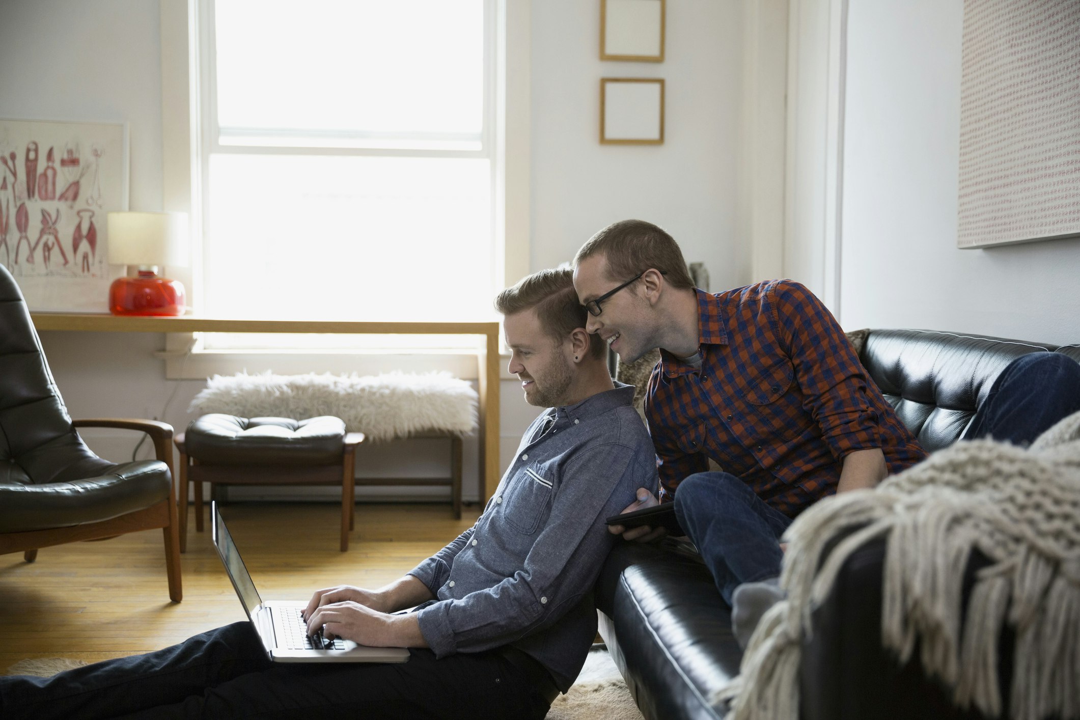A homosexual couple sitting in their living room and looking at a computer
