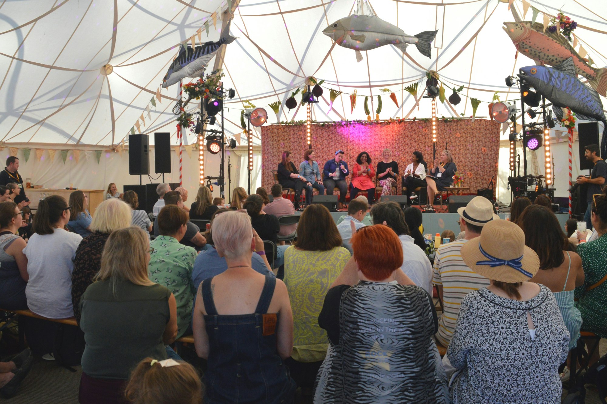A panel of speakers on a stage address a crowd inside a bell tent.