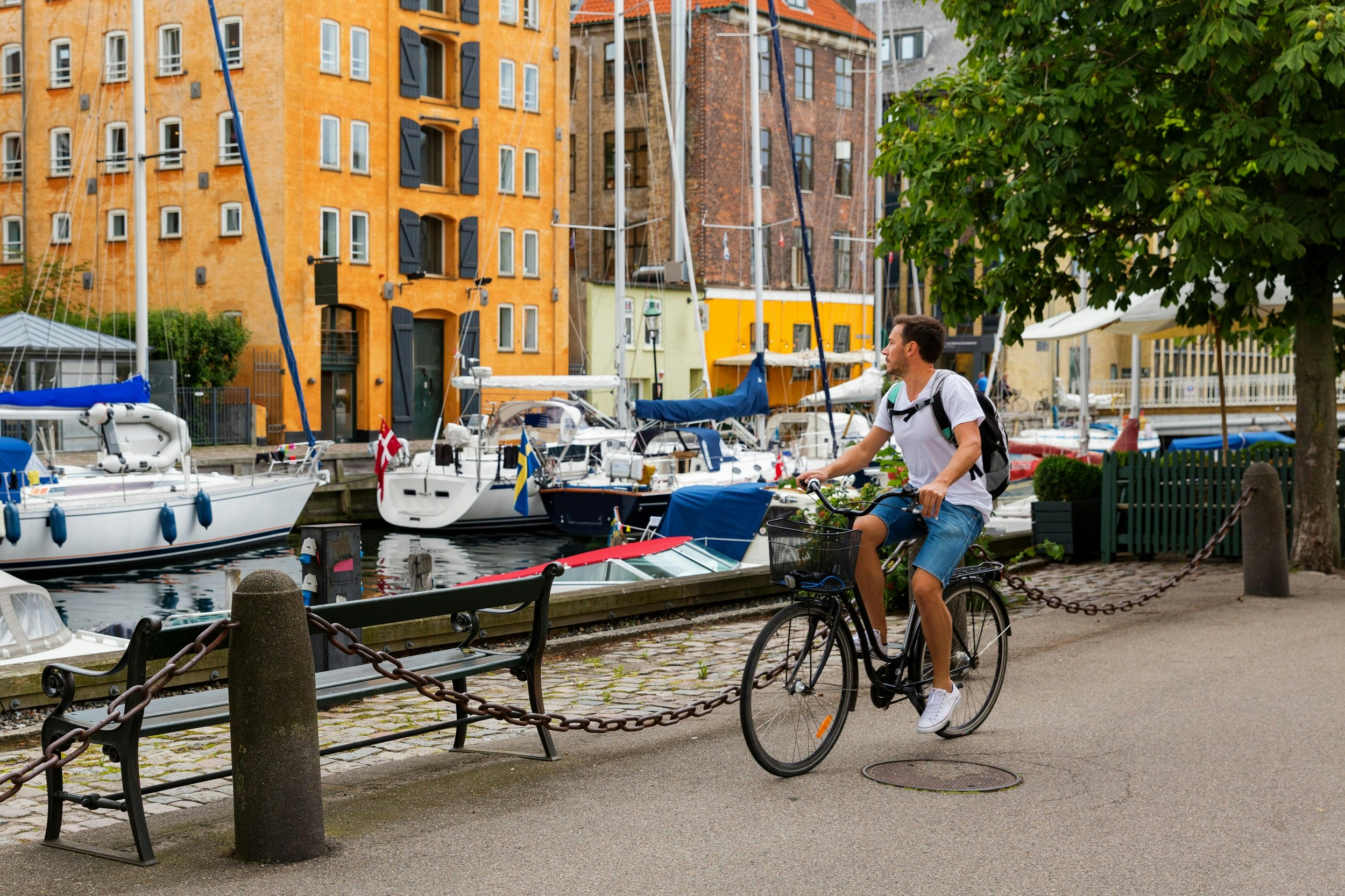A male cyclist rides alongside a picturesque canal, with many small boats docked there.