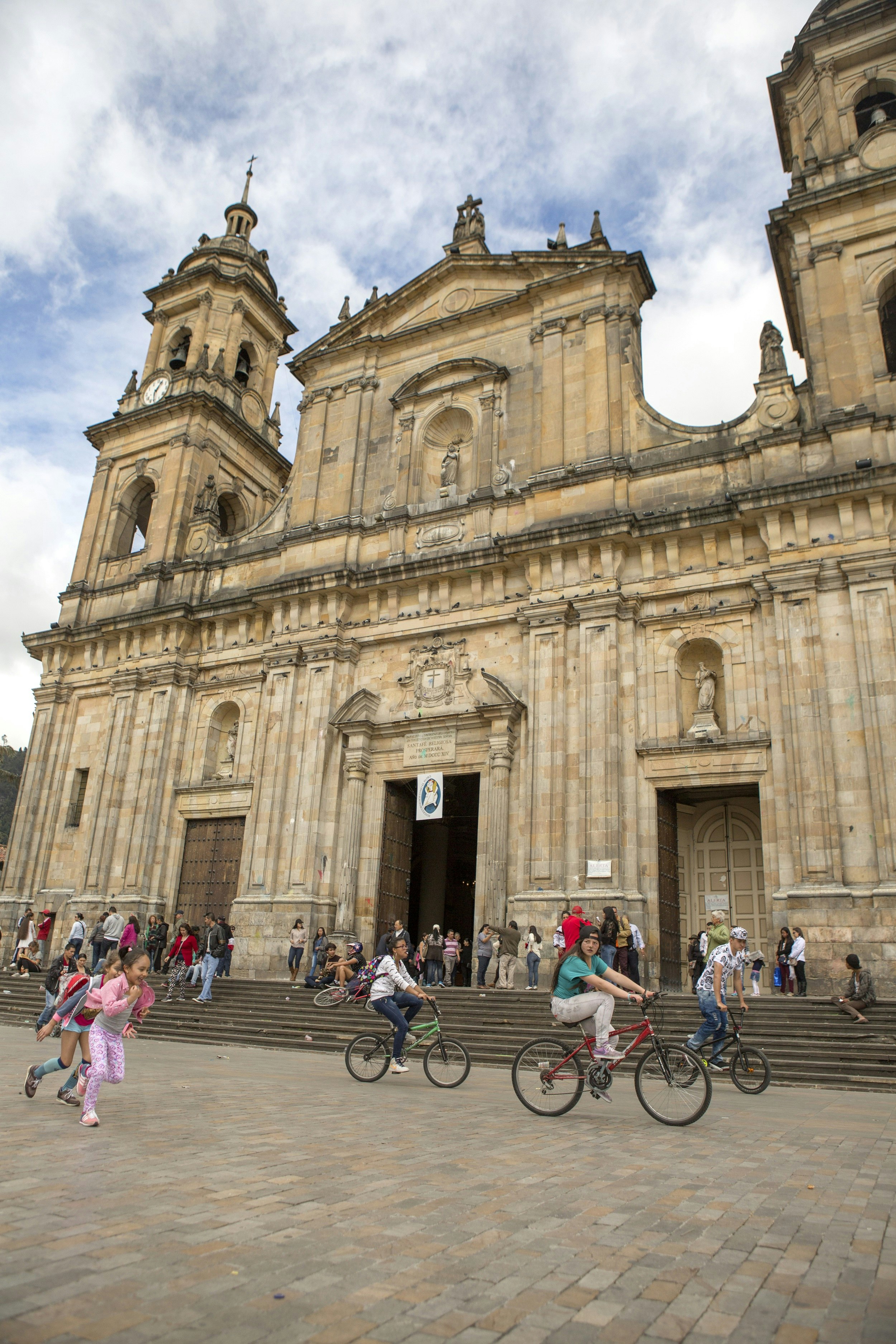 Some young children on bikes cycle past La Catedral Primada in the city's main plaza