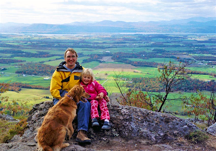 A man and a young girl sit on an overlook on a mountain in Vermont; kids outdoor adventures
