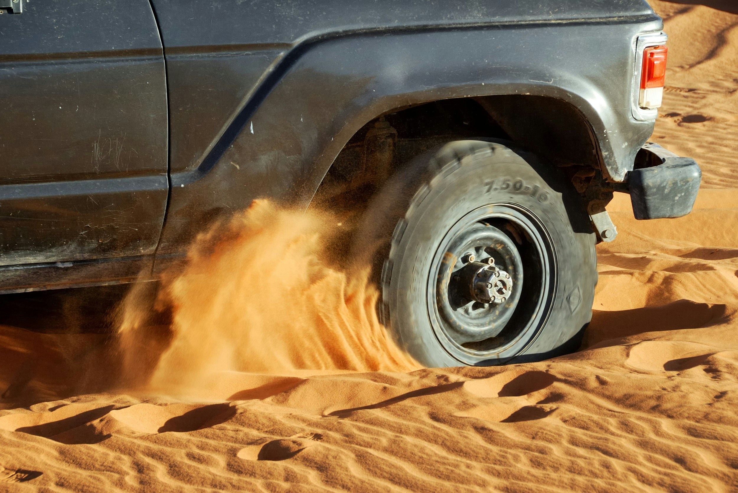 The front wheel of a Toyota Land Cruiser spins in deep sand, throwing it everywhere.