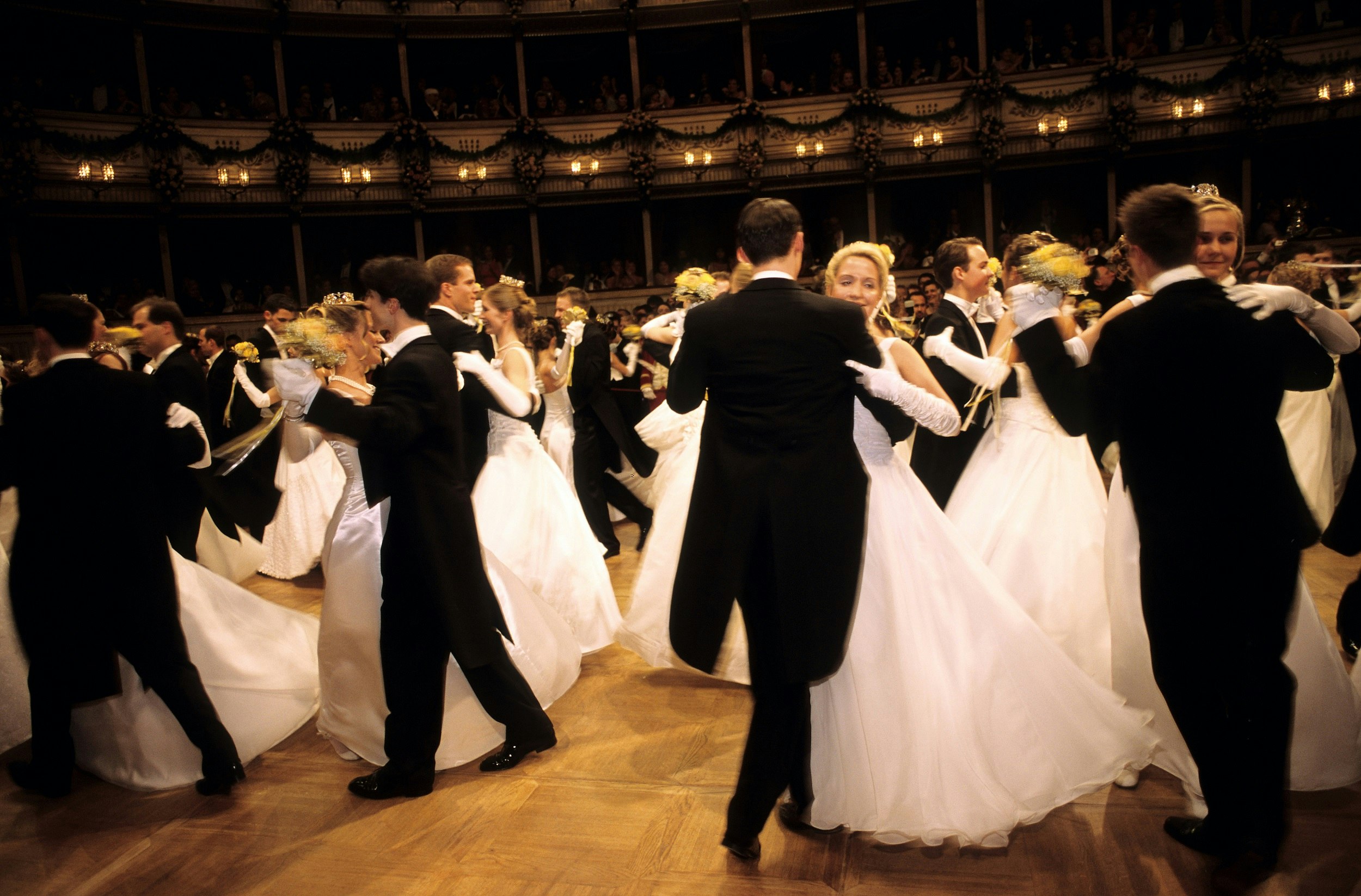 A blur of dancers moves around the dance floor, with men wearing black suits and women in white dresses