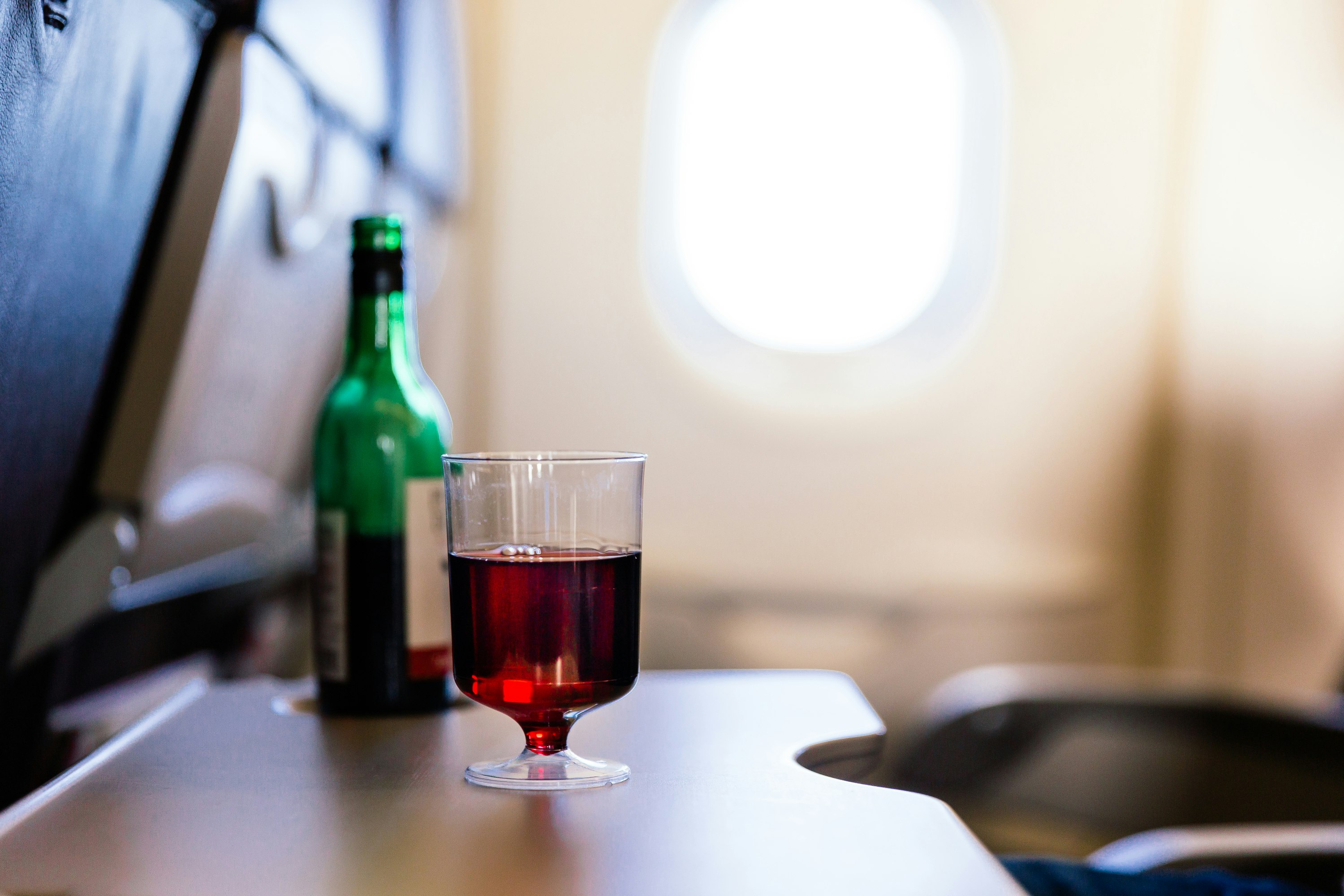A glass of red wine sits on an airplane tray table. 