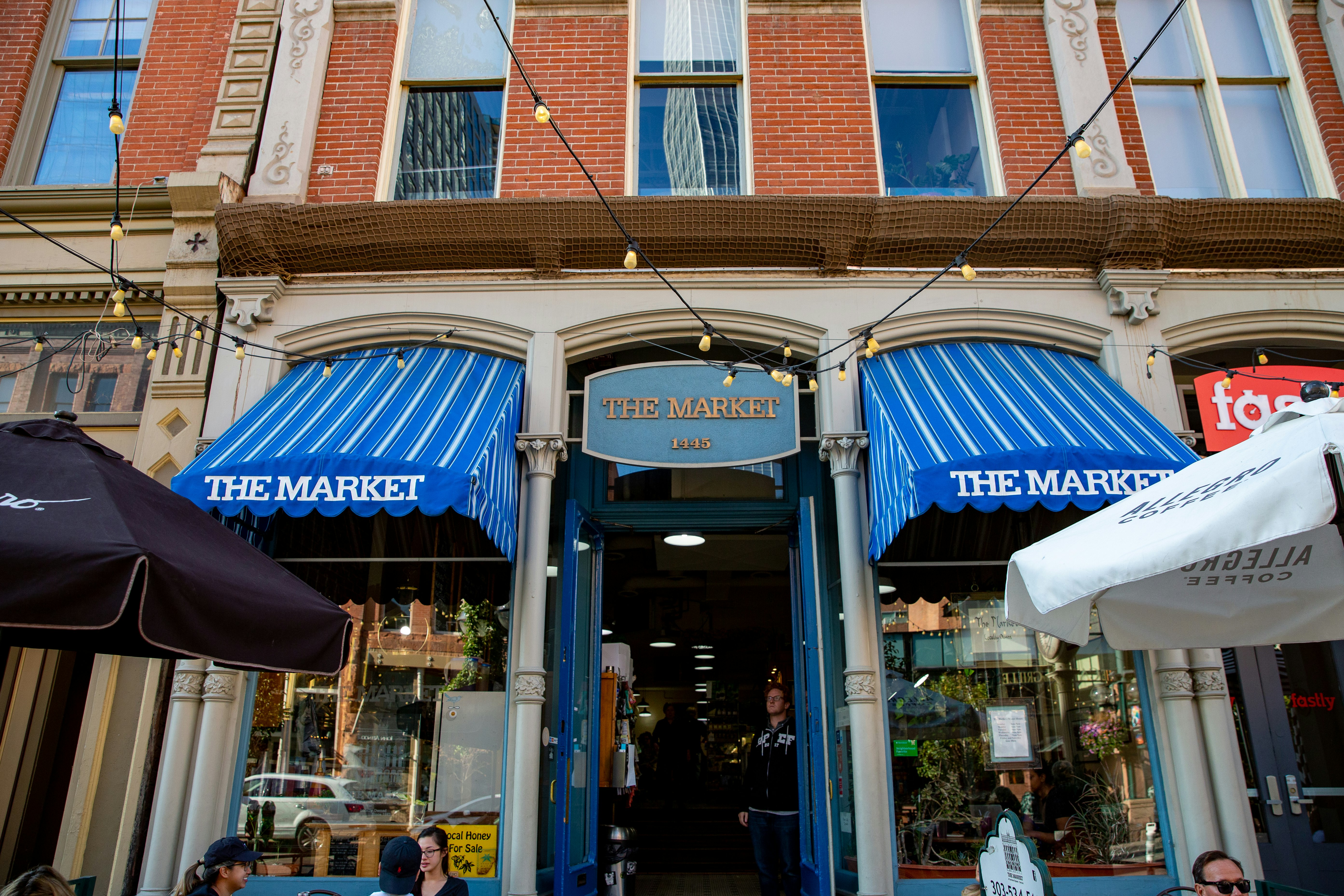 A Victorian brick facade with grey columns with Corinthian caps and blue awnings with white stripes, which say "The Market" in white letters on the fronts. A metal sign over the doorway between the columns also reads "The Market"
