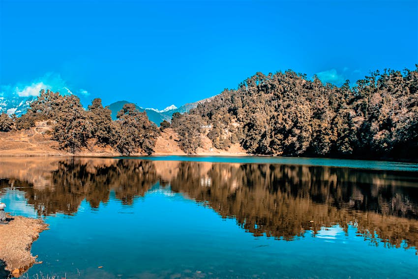 Ένας λαμπερός μπλε ουρανός αντανακλάται σε μια καθαρή λίμνη που περιβάλλεται από σκονισμένους καφέ λόφους και εξίσου γκριζοκαφέ φύλλωμα δέντρων.