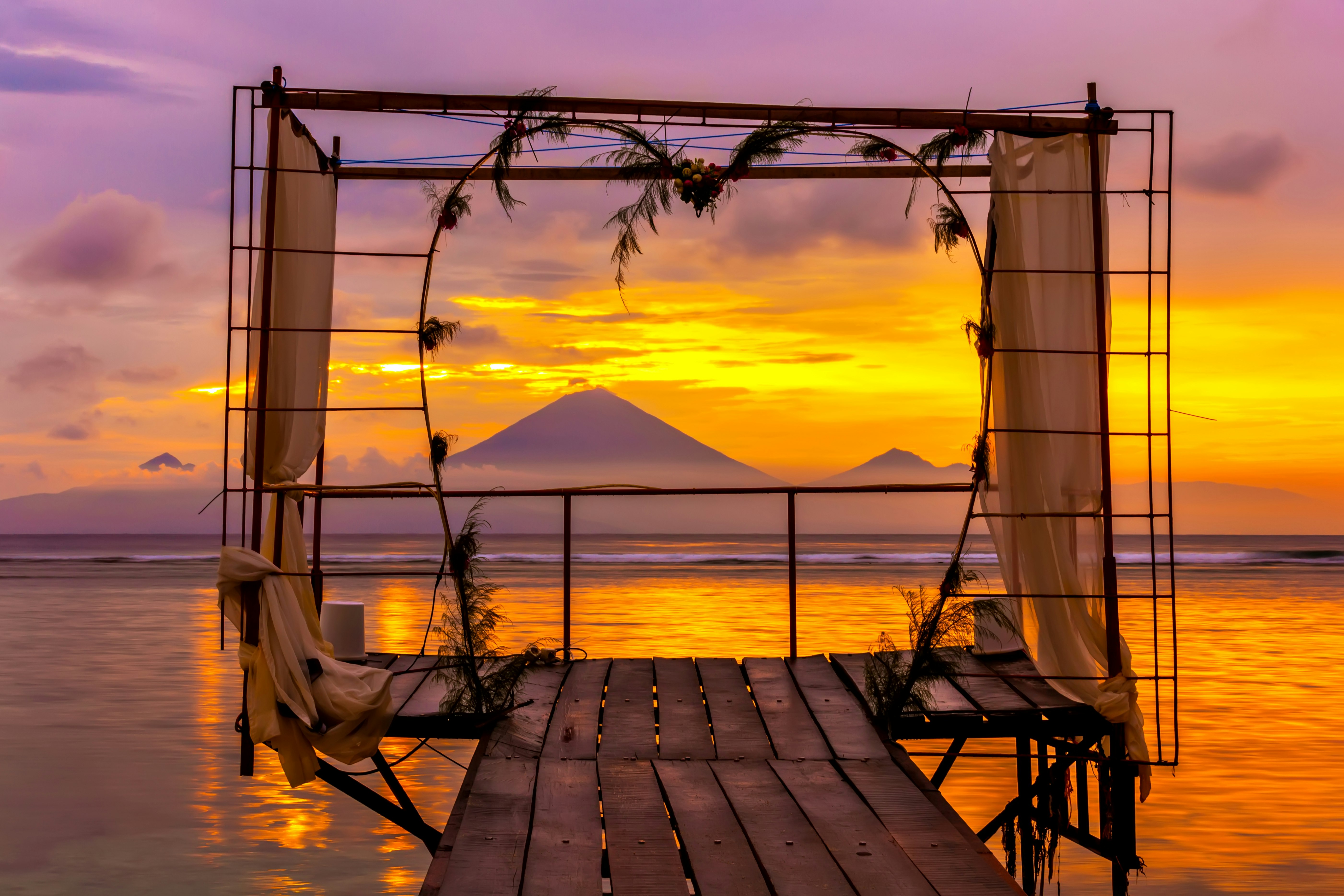 A sunset scene of a rustic wire altar on a jetty jutting out over the water in the Gili Islands, Lombok.