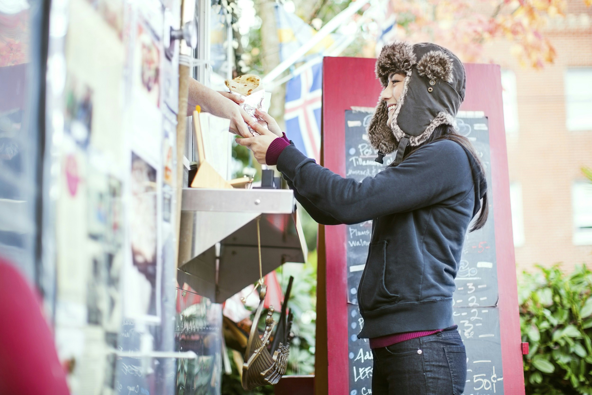 A smiling woman grabs a foil-wrapped meal from the hands of a vendor who is leaning out of a food truck.