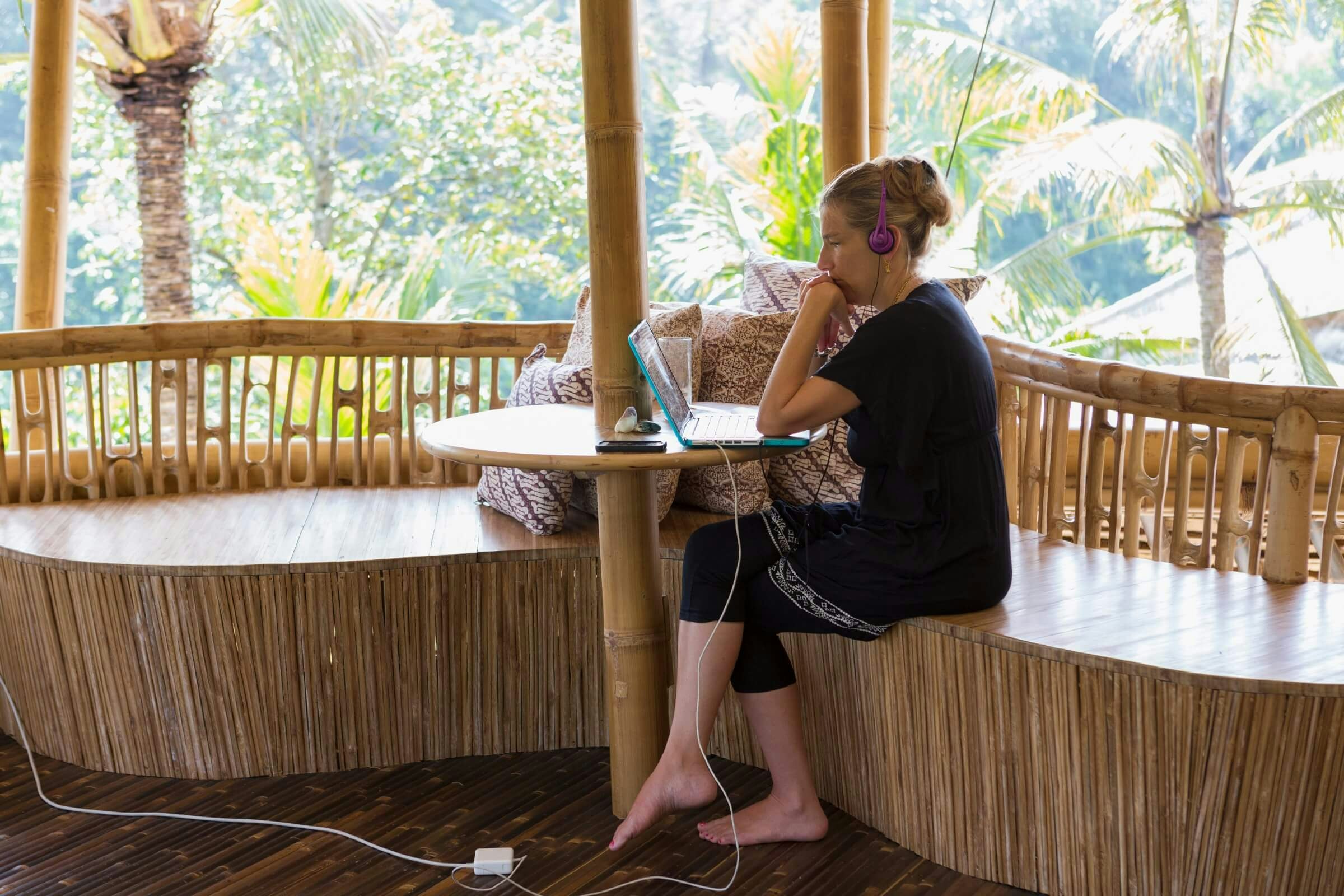 A woman using a laptop and headphones on a bamboo patio on a sunny day