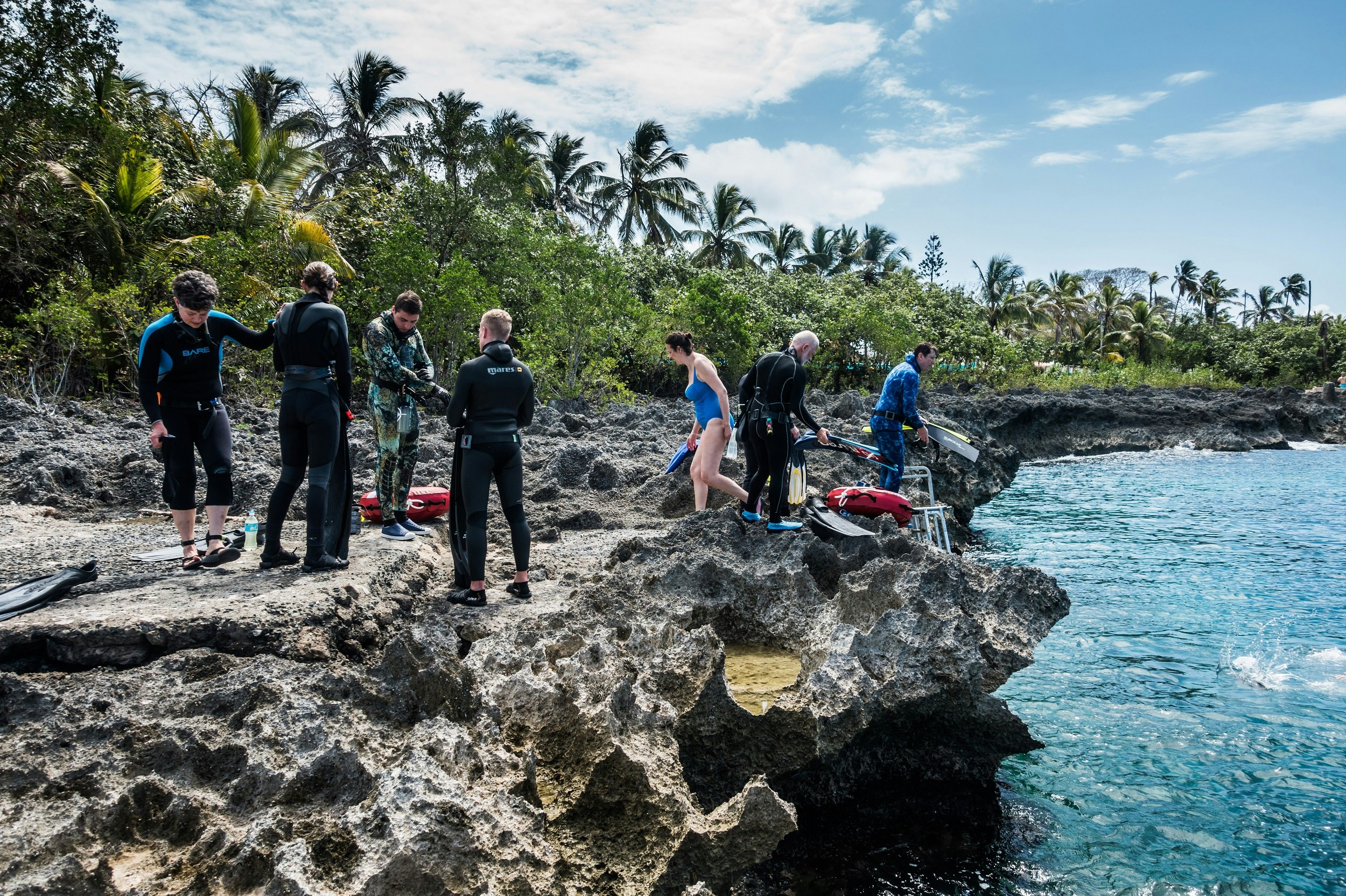A group of free divers stands on a rocky outcrop that teeters out over the ocean; they are preparing to enter the water on the rocky shore of San Andres Island.