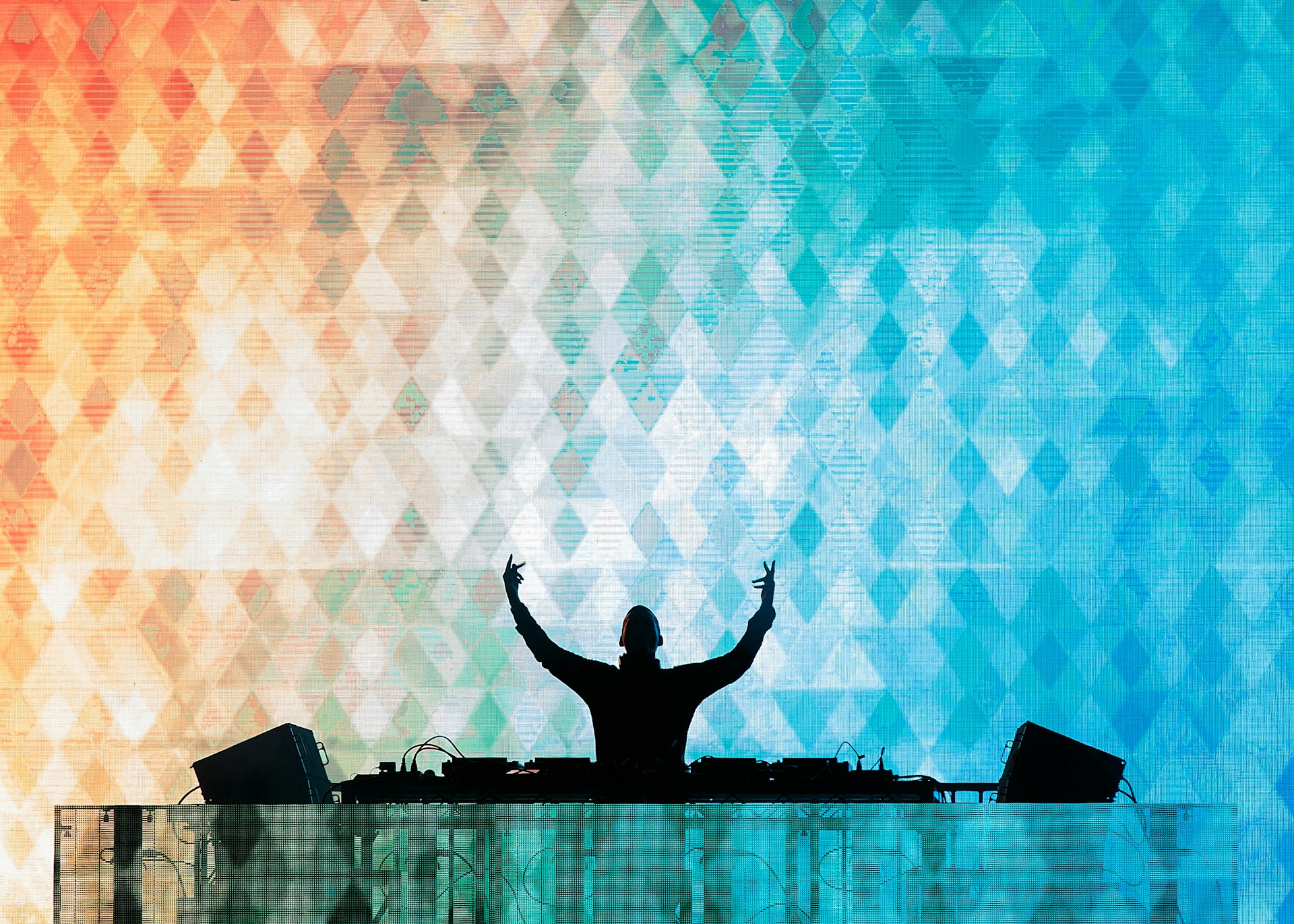 A DJ puts his hands in the air in front of a colorful light display