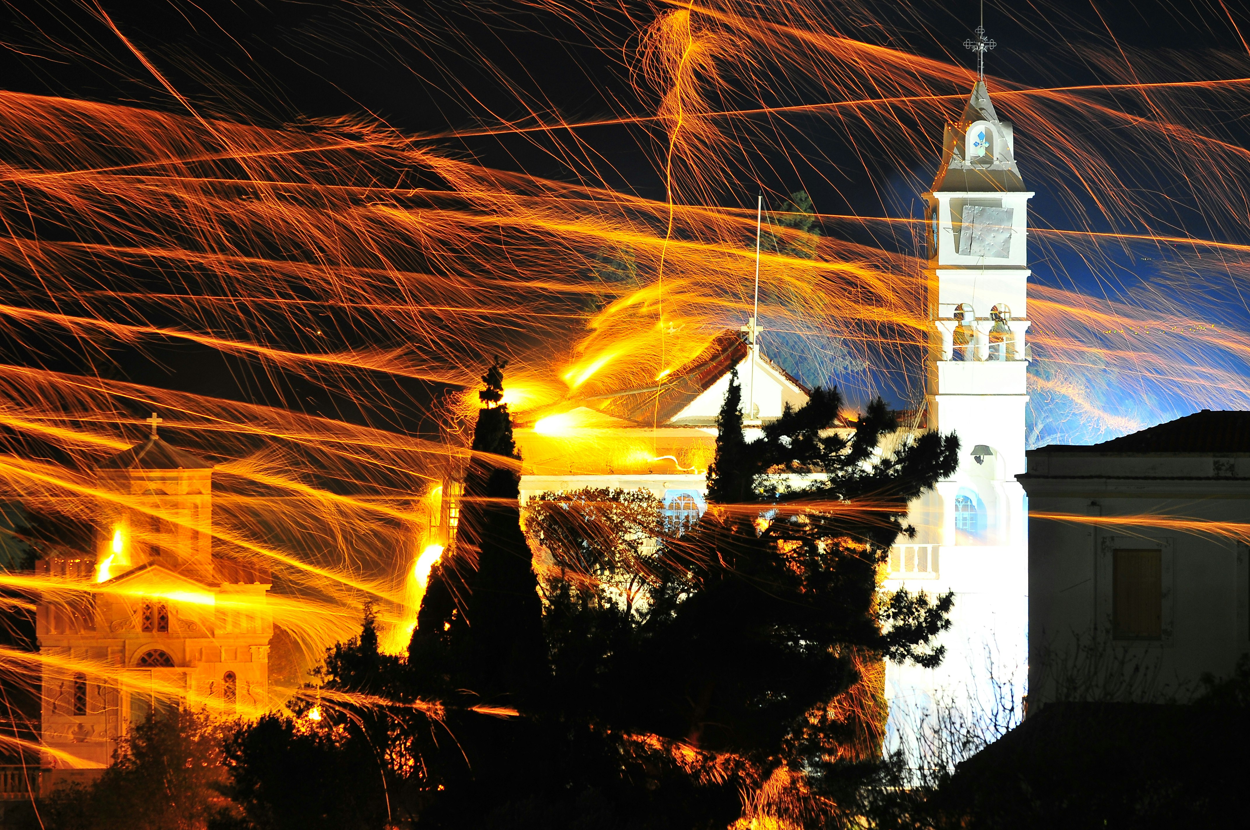 A night-time long-exposure shot showing the glowing paths of rockets attacking a church during 'rouketopolemos' on the island of Chios, Greece.