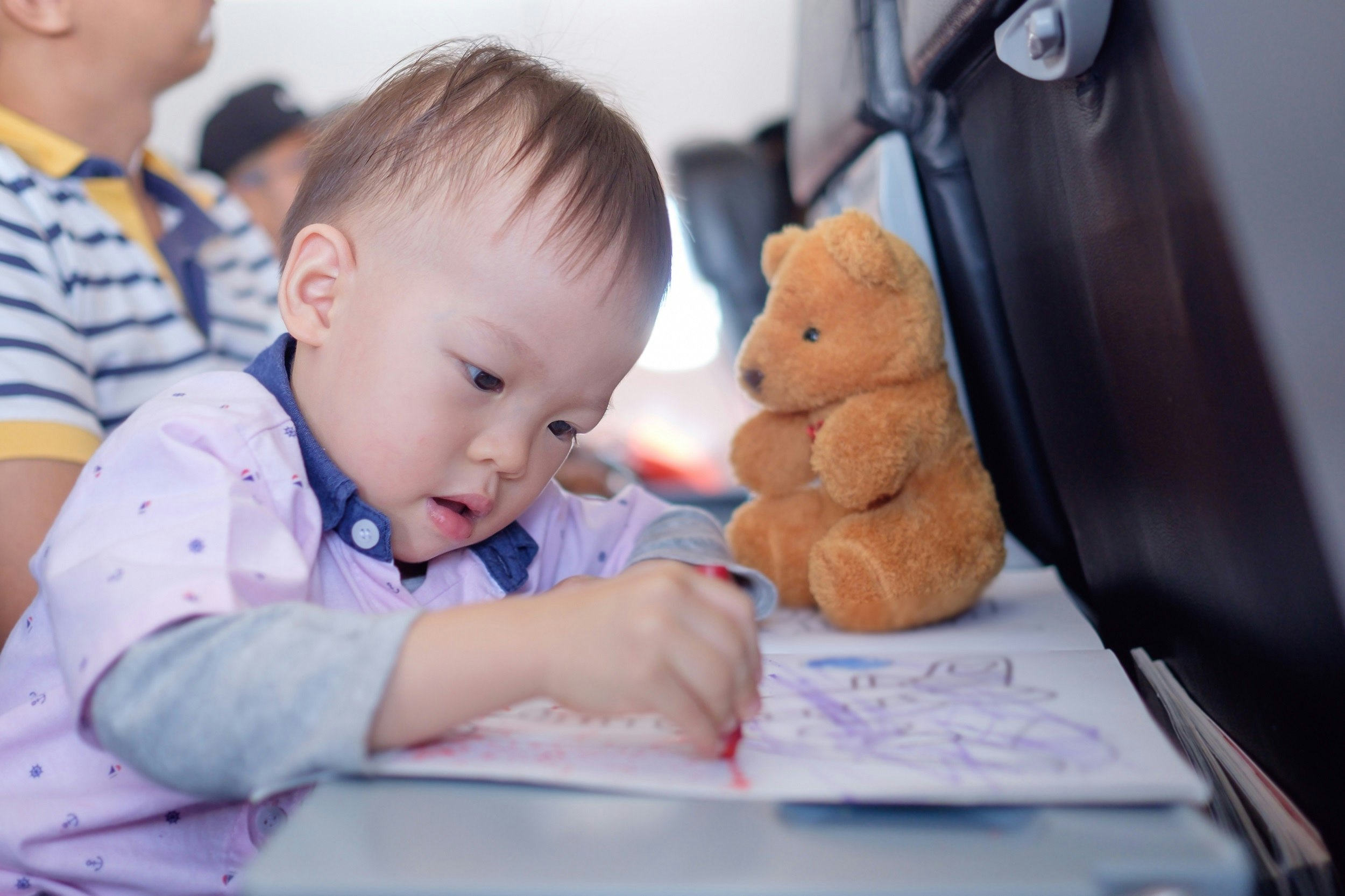 A toddler does some colouring on the table in an economy seat on a plane