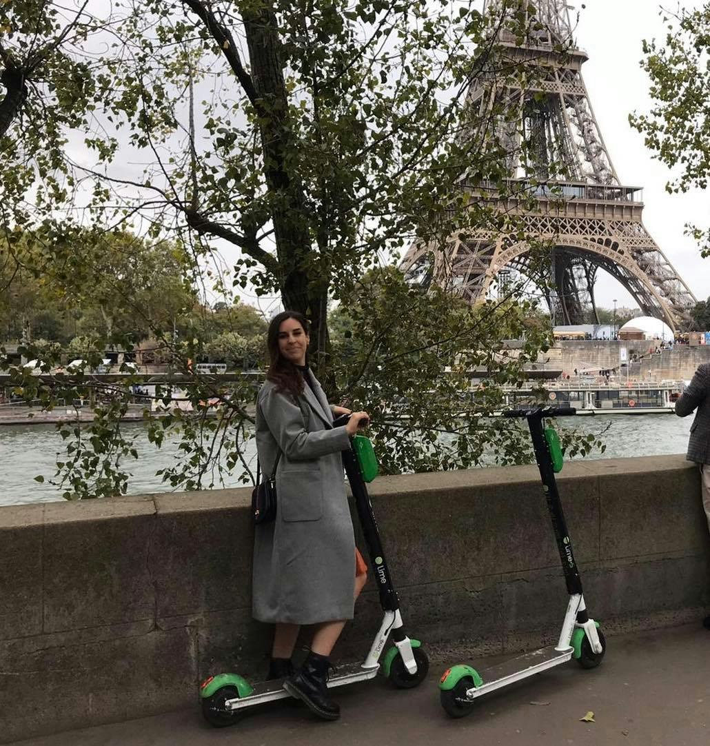 The author hops on a green scooter with the Eiffel Tower and River Seine in the background