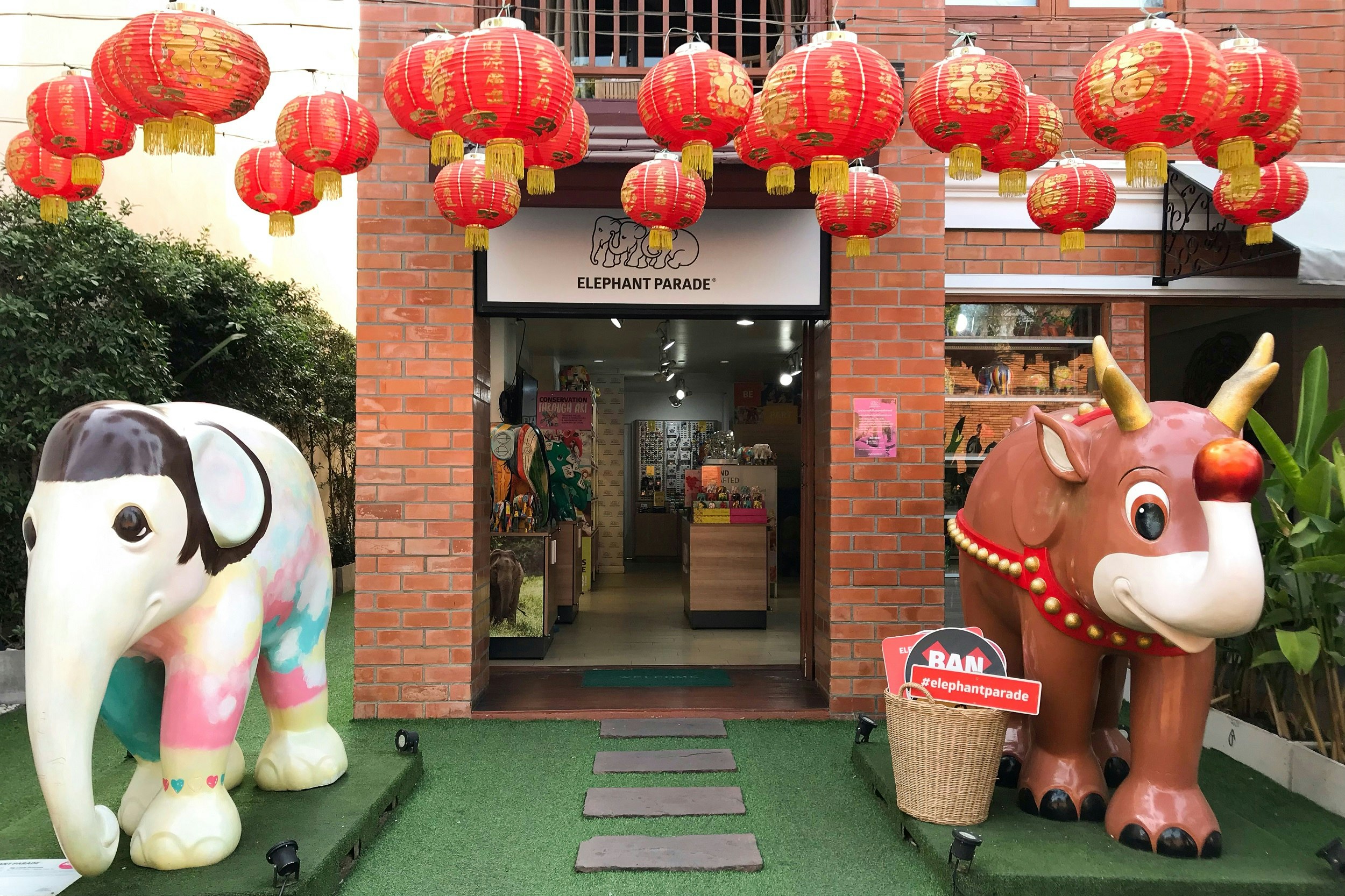 The doorway to a shop flanked by two large elephant sculptures. Above hang red paper lanterns covered in golden writing.