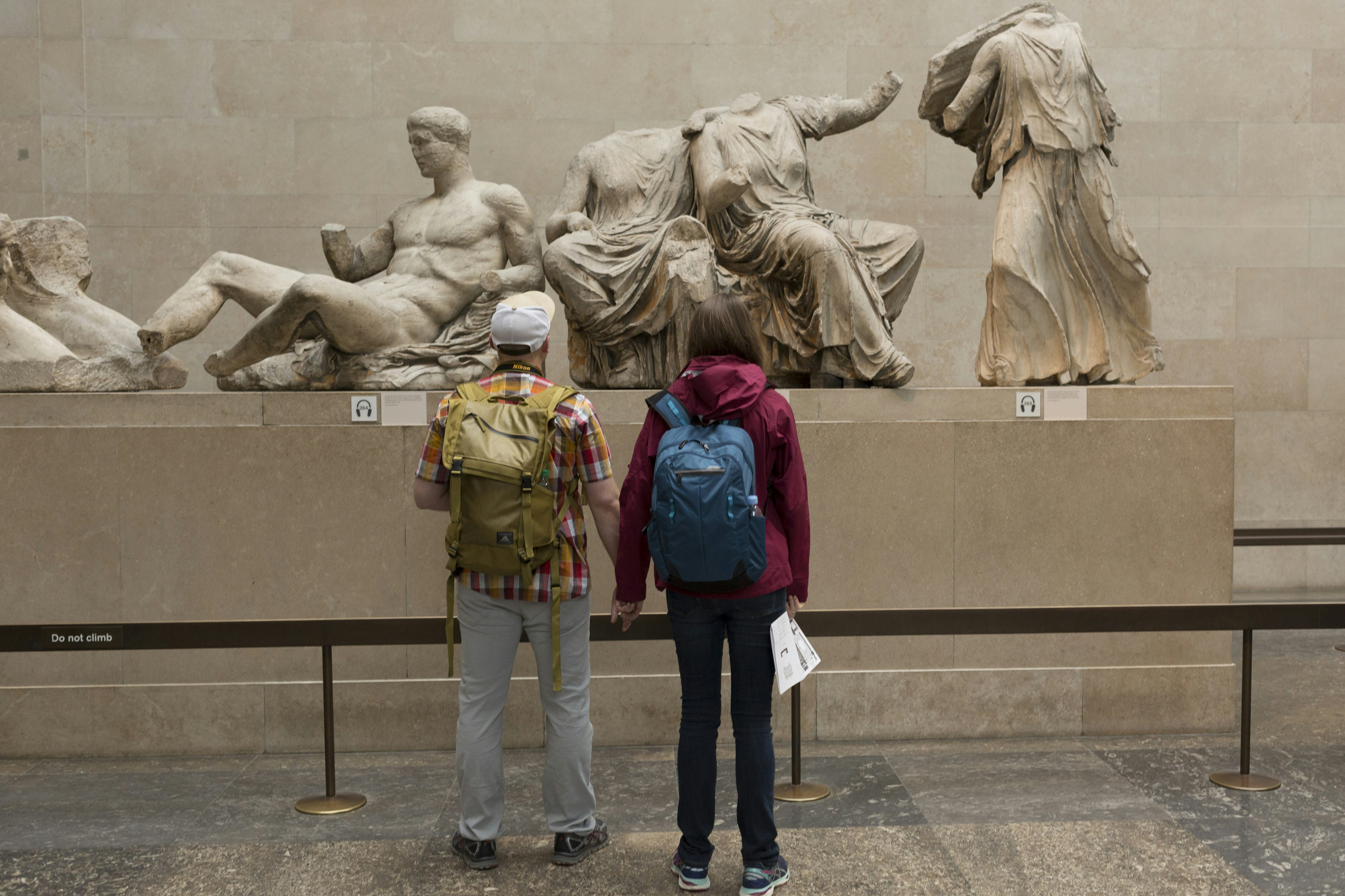 A pair of tourists stand in front of the Parthenon Marbles Metopes in the British Musem