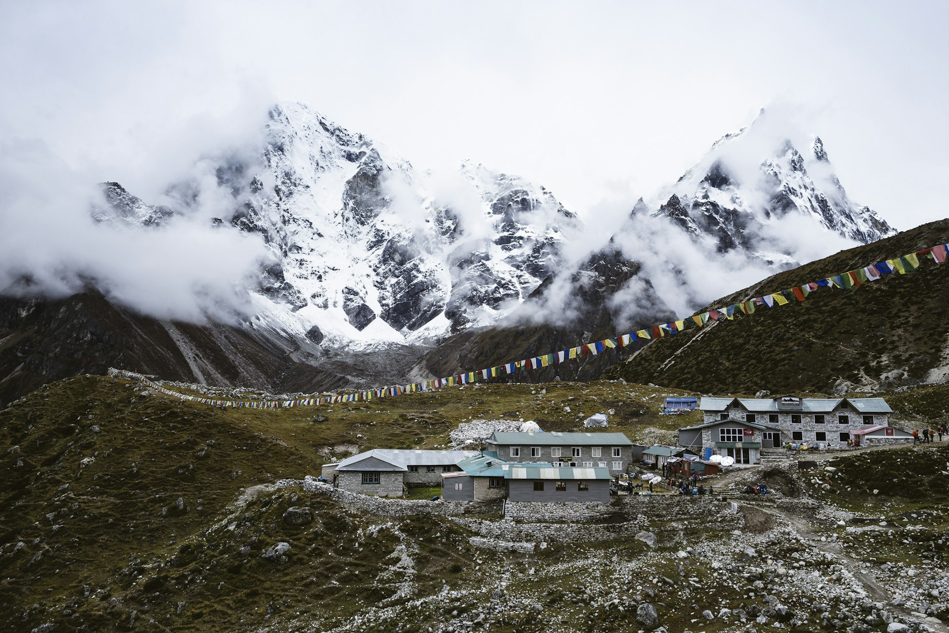 The village of Dughla sits on a rocky outcropping covered in short alpine grass with dramatic Himalayan peaks in the background 