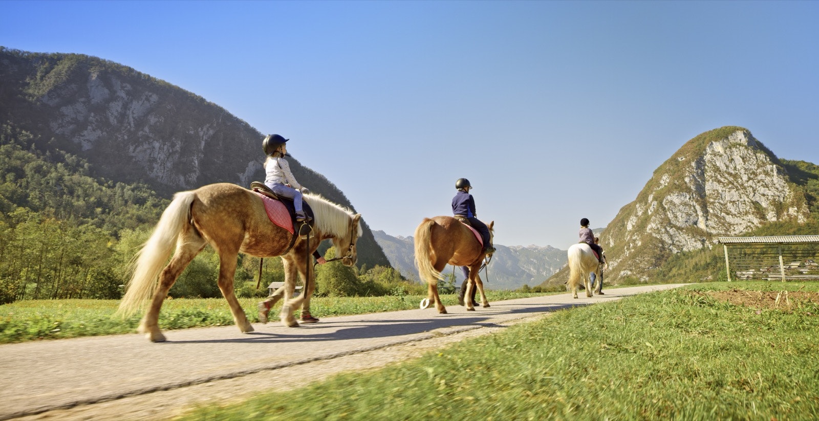 Three horses with riders of different ages walk in a line toward some hills