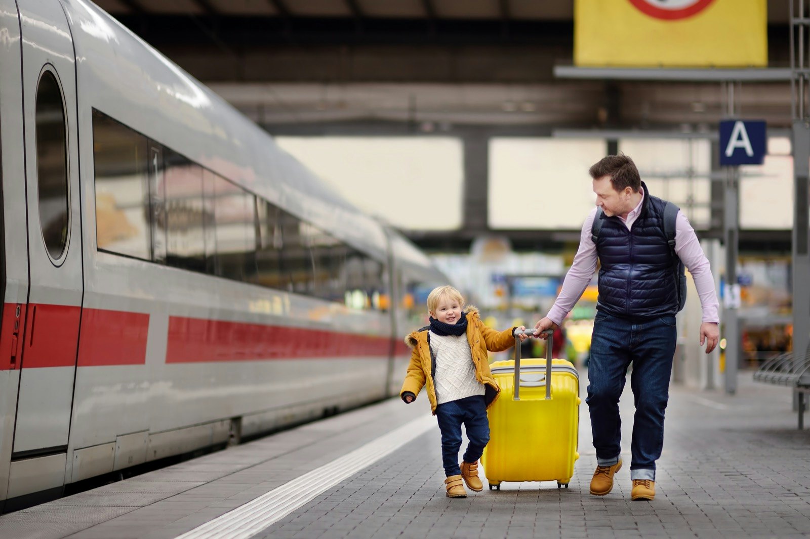 father and son pull a big yellow suitcase on a train platform