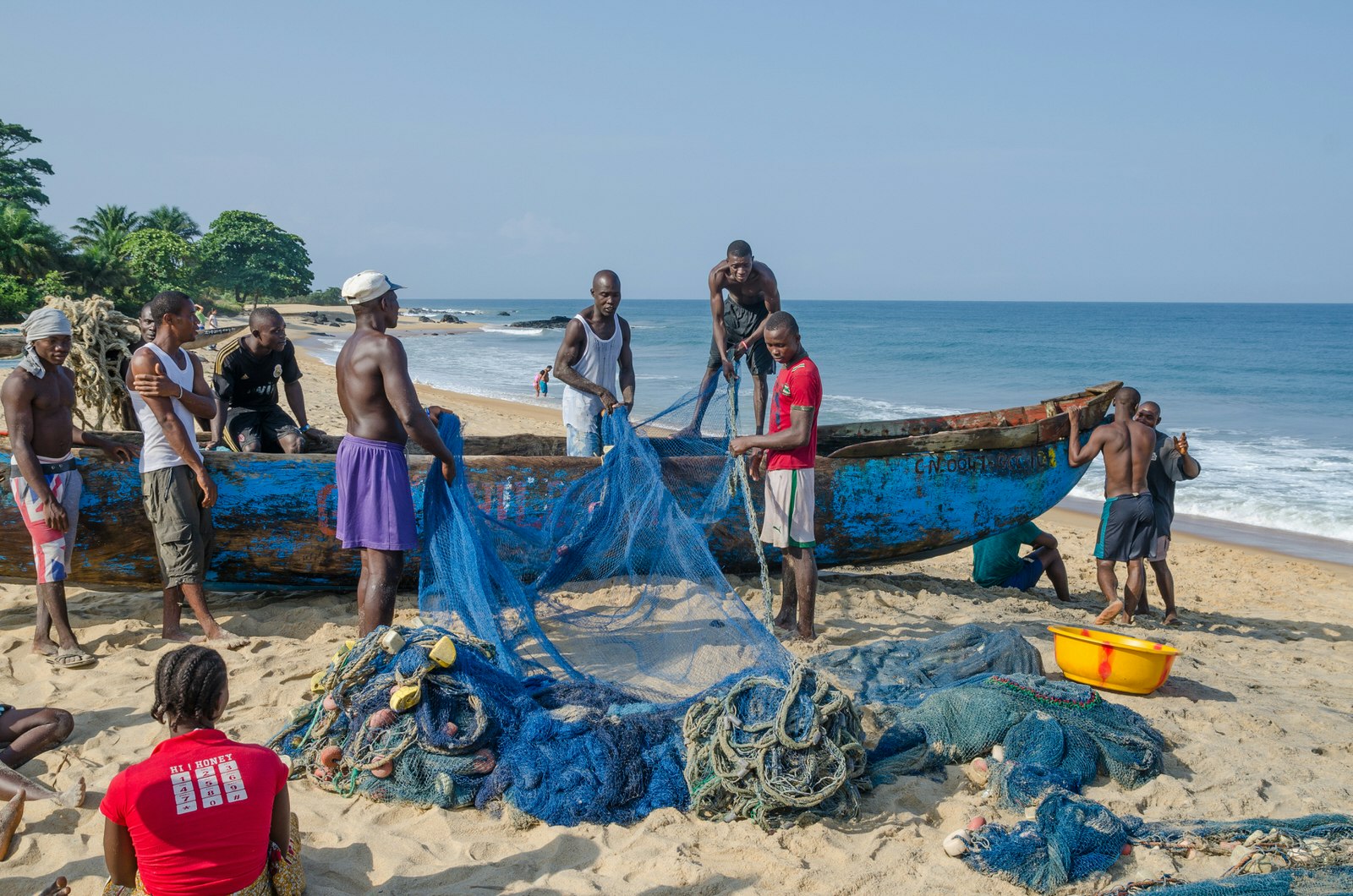 A group of fishers work to load their nets onto their traditional long canoe on the beach