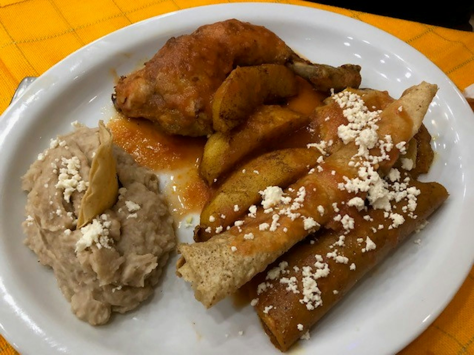 A white plate which is piled with a chicken leg, potato wedges, fluffy rolled-up tortillas and a thick beige sauce.