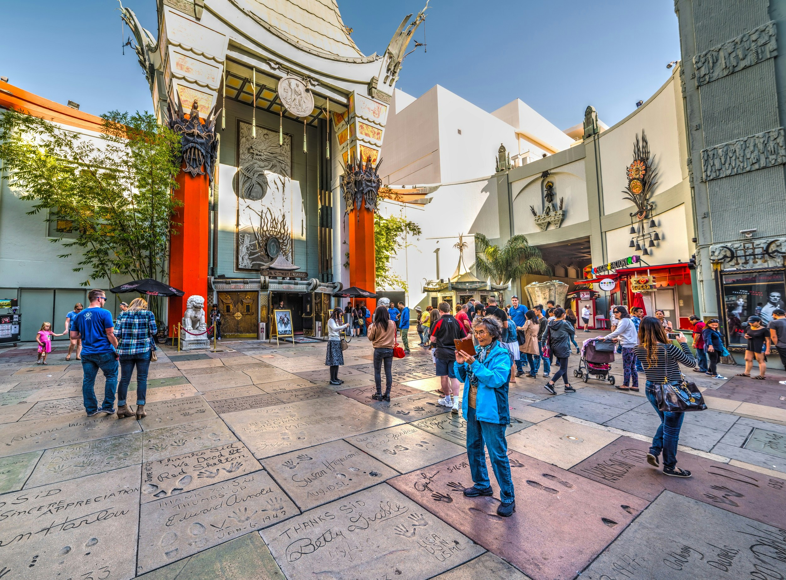 People mingle on the pavement outside the grand TCL Chinese Theater, which resembles a Chinese temple; the pavement is made of slabs of concrete with the handprints and footprints of celebrities.