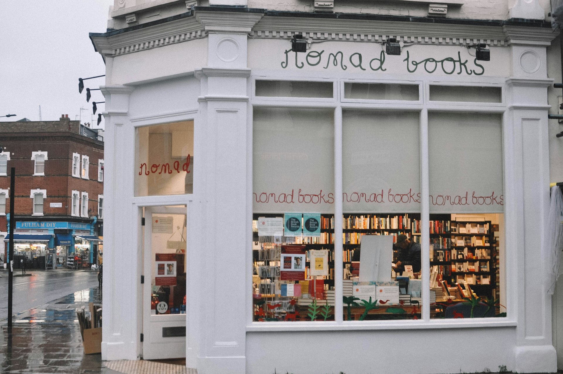 Nomad Books white facade. Inside the lights are on and a man is browsing books.