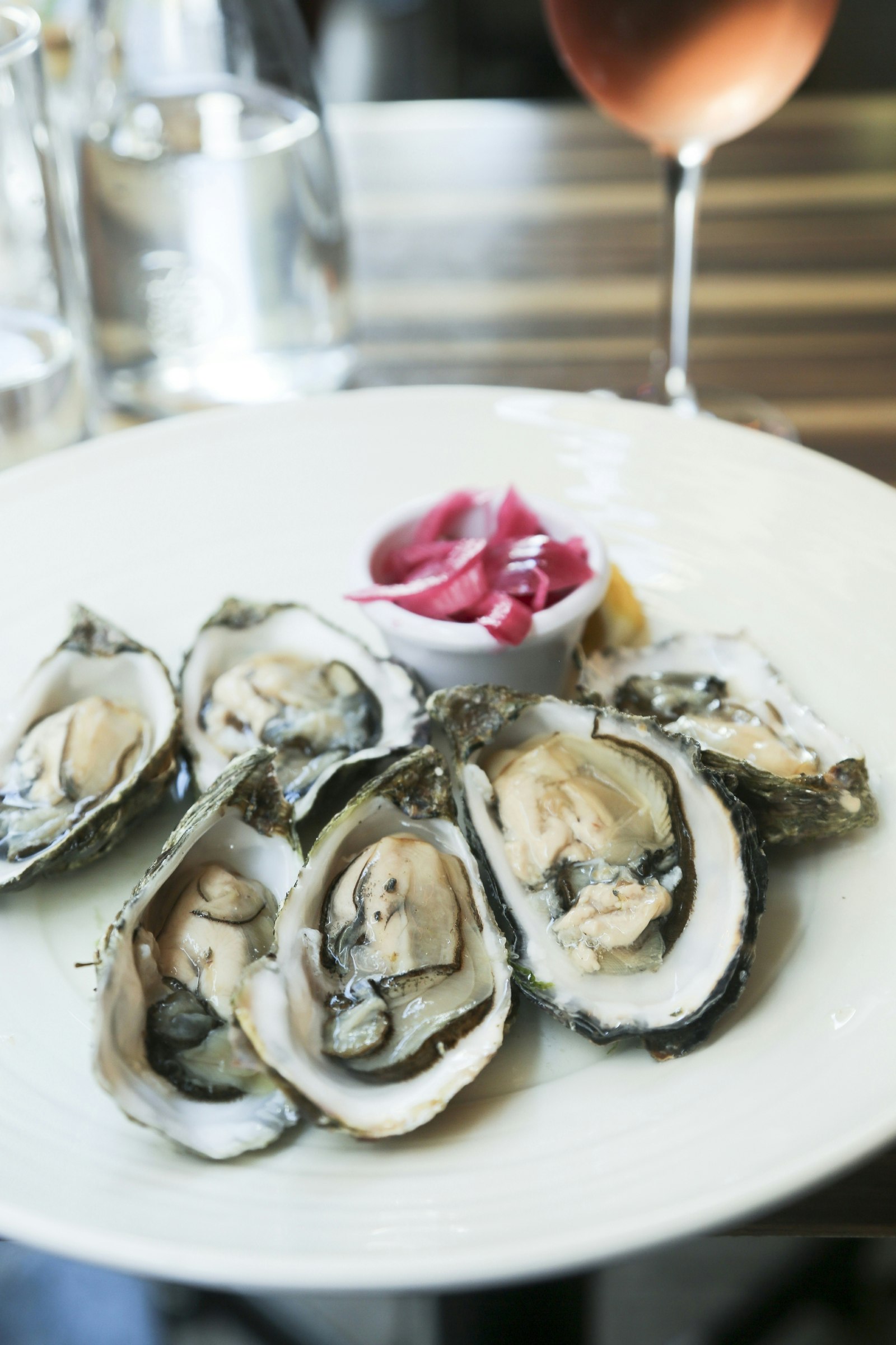 A plate of oysters with a chilled glass of rose in the background