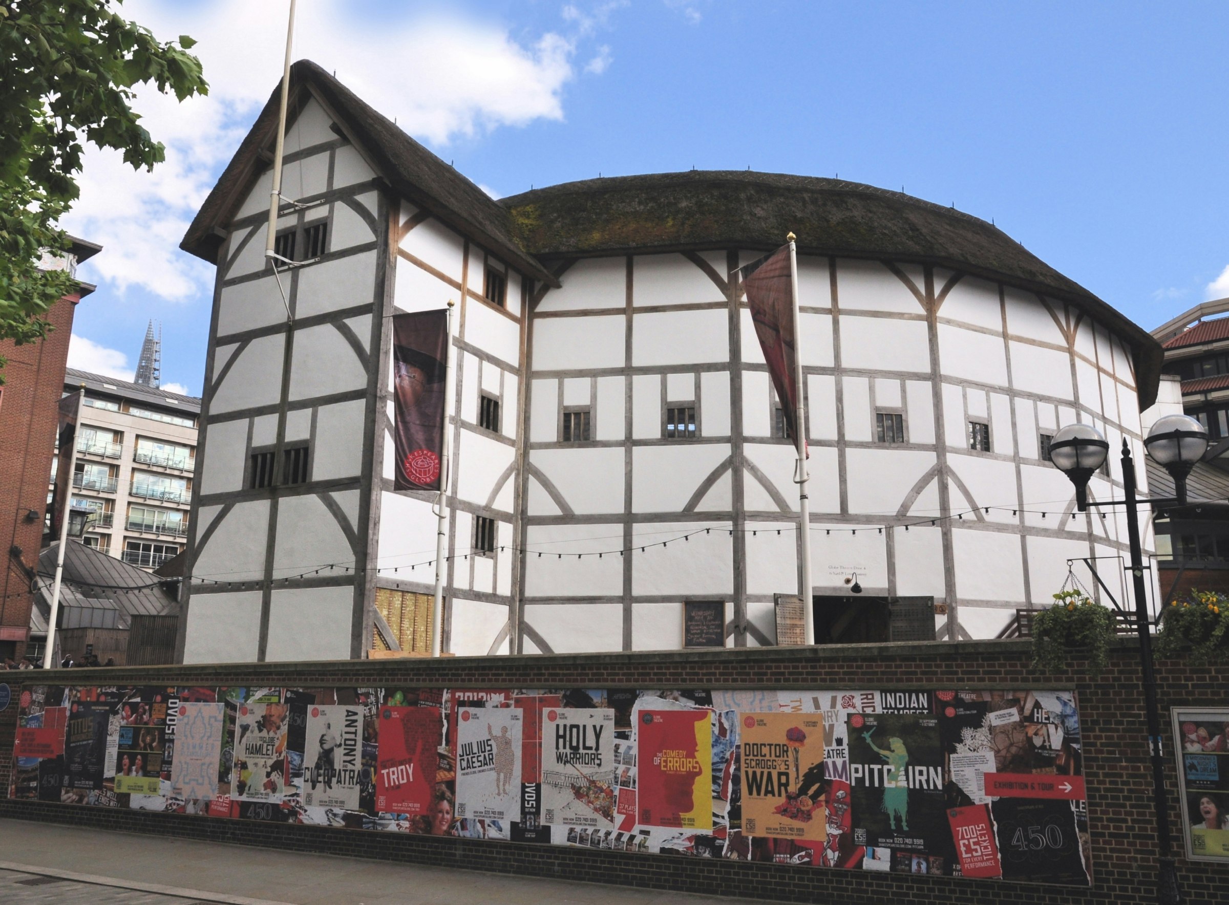 The exterior of Shakespeare's Globe Theatre in London, a reconstruction of the original with a thatched roof and exposed wooden beams bathed in sunlight