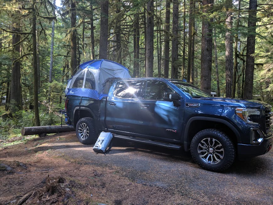 En mörkblå 2019 GMC Sierra-lastbil med ett ljusare blått och grått lastbilstält monterat i sängen sitter i en grön skog i delstaten Washington