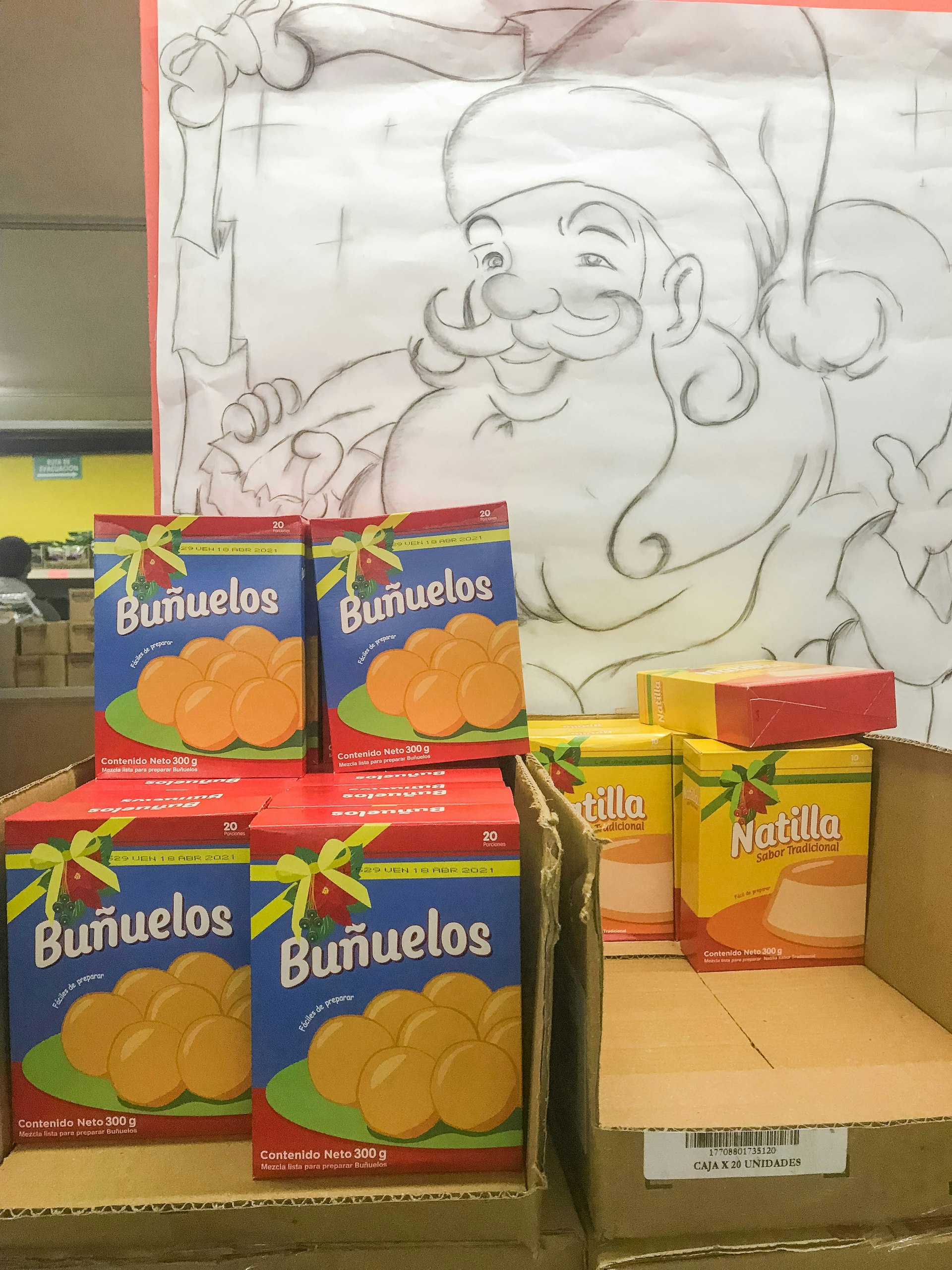 A hand-drawn sketch of Santa in pencil presides over blue and red boxes of Buñuelos and yellow boxes Natillas, both with Christmas ribbons and holly on their packaging. 