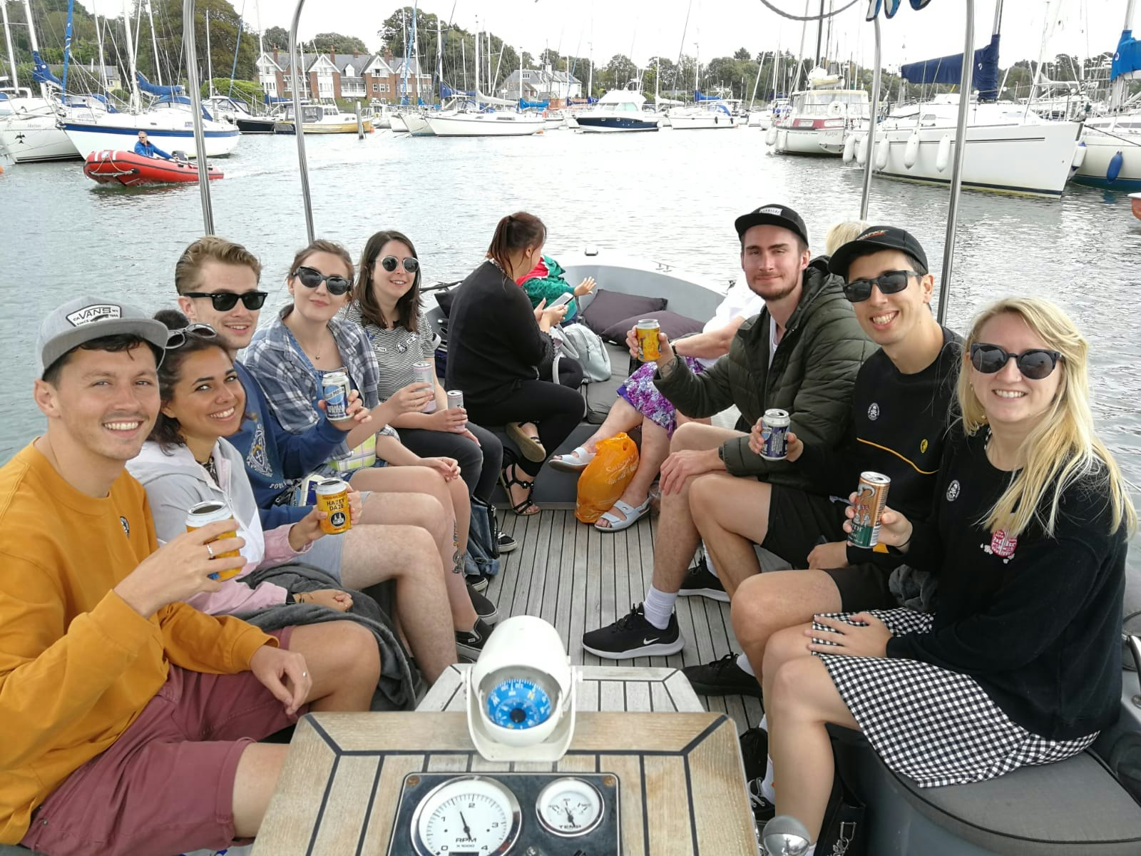 A group of 8 friends sit holding beers in a boat. New Forest spending diary