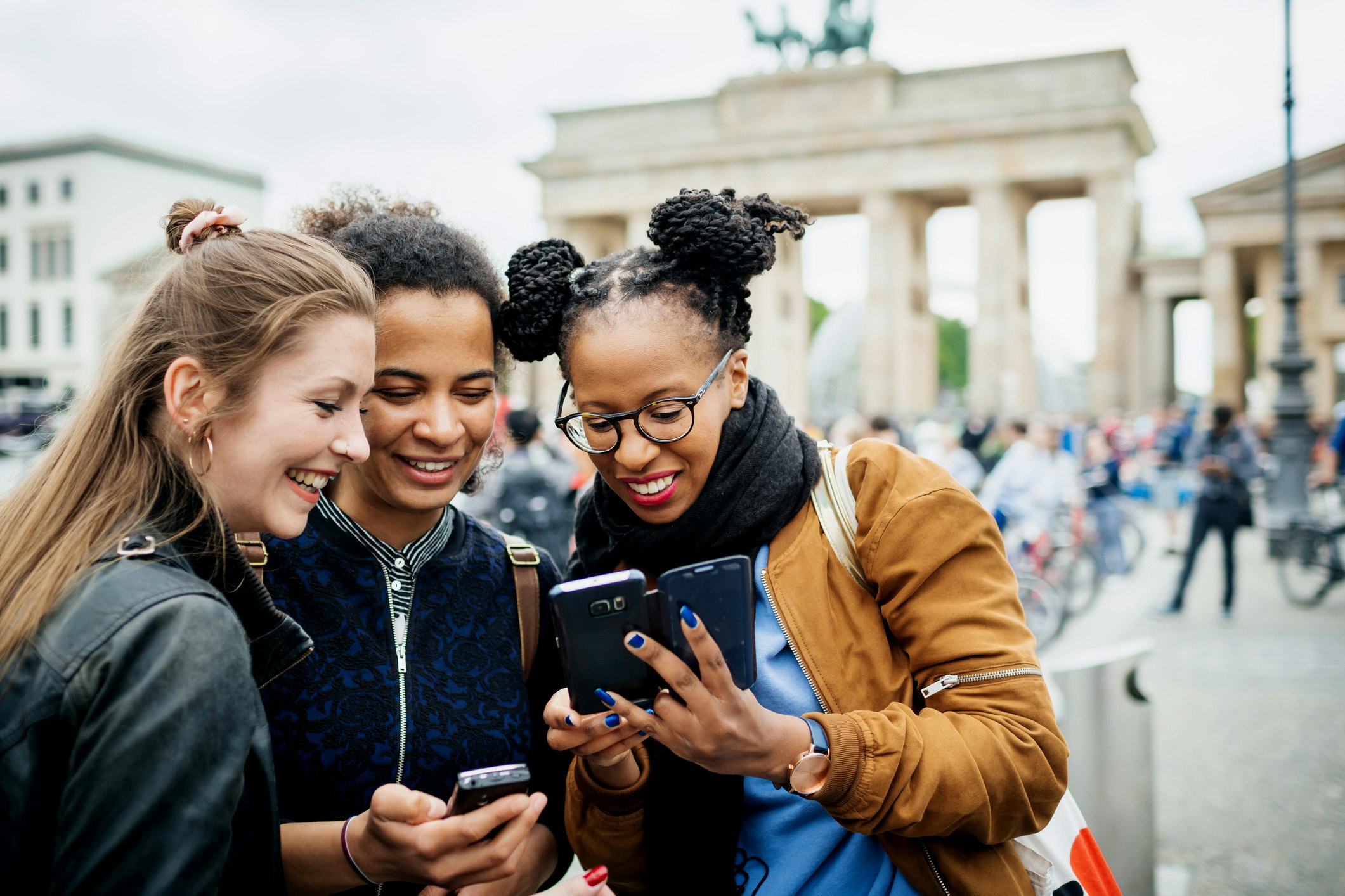 A group of girls looking at a photo next to Berlin's Brandenburg Gate