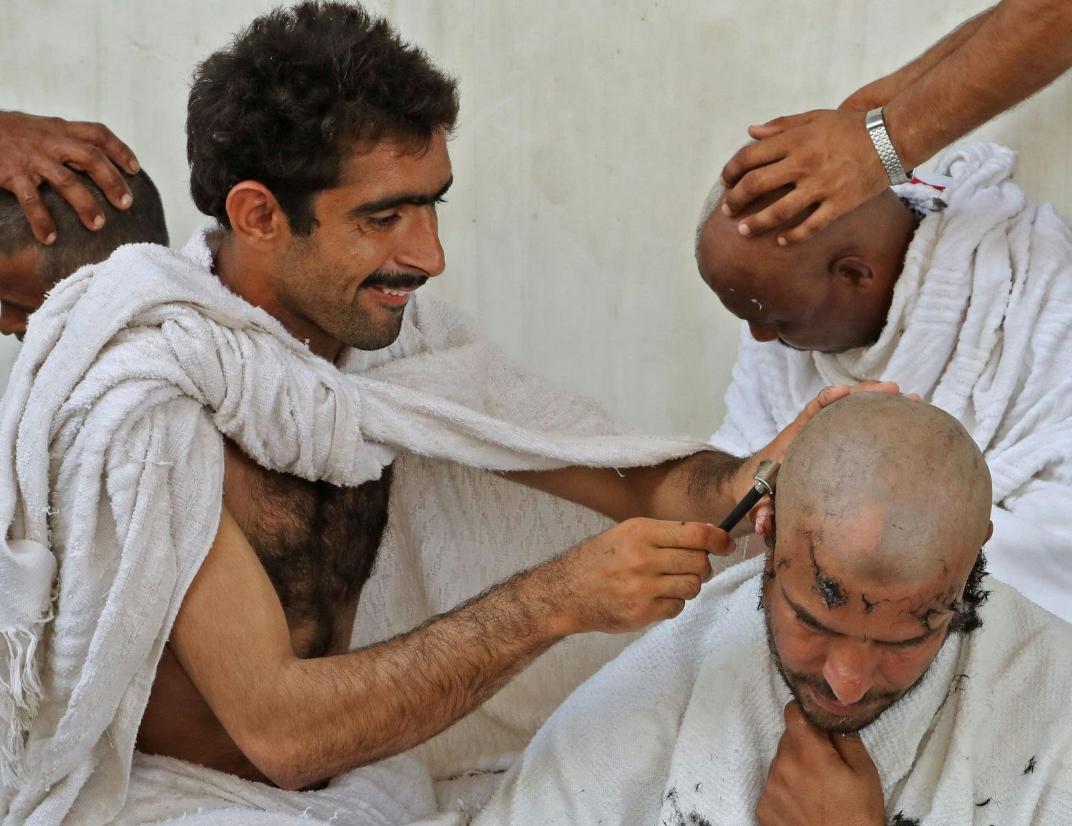 Three Muslim men having their heads shaved by long-blade razors.