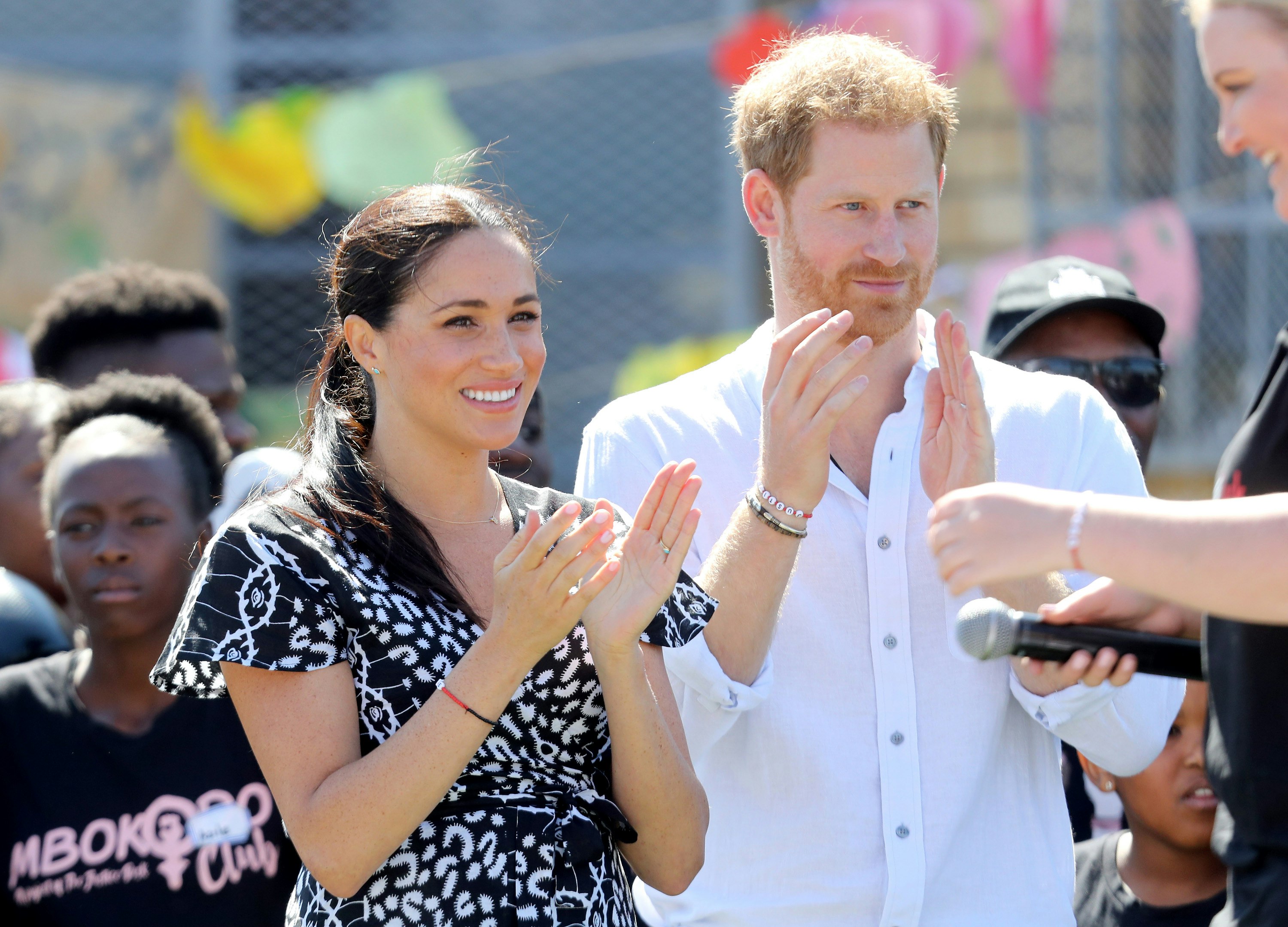 Meghan Markle and Prince Harry stand side by side, clapping as they look on at a performance. 