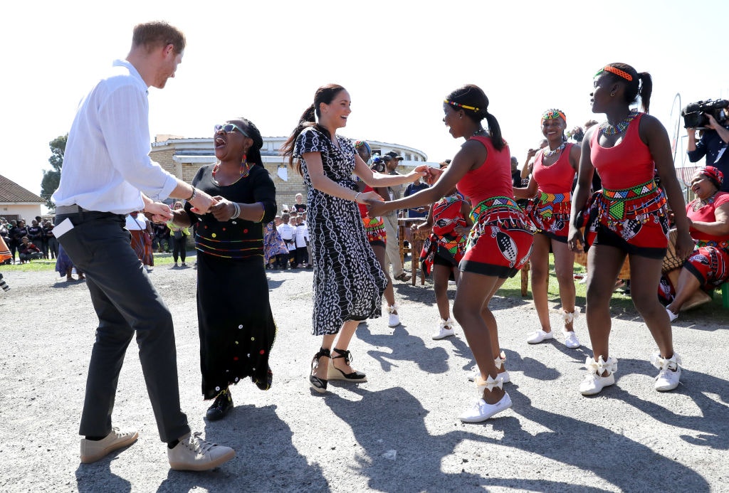 Prince Harry dances with a woman while his wife Meghan dances with some girls. 