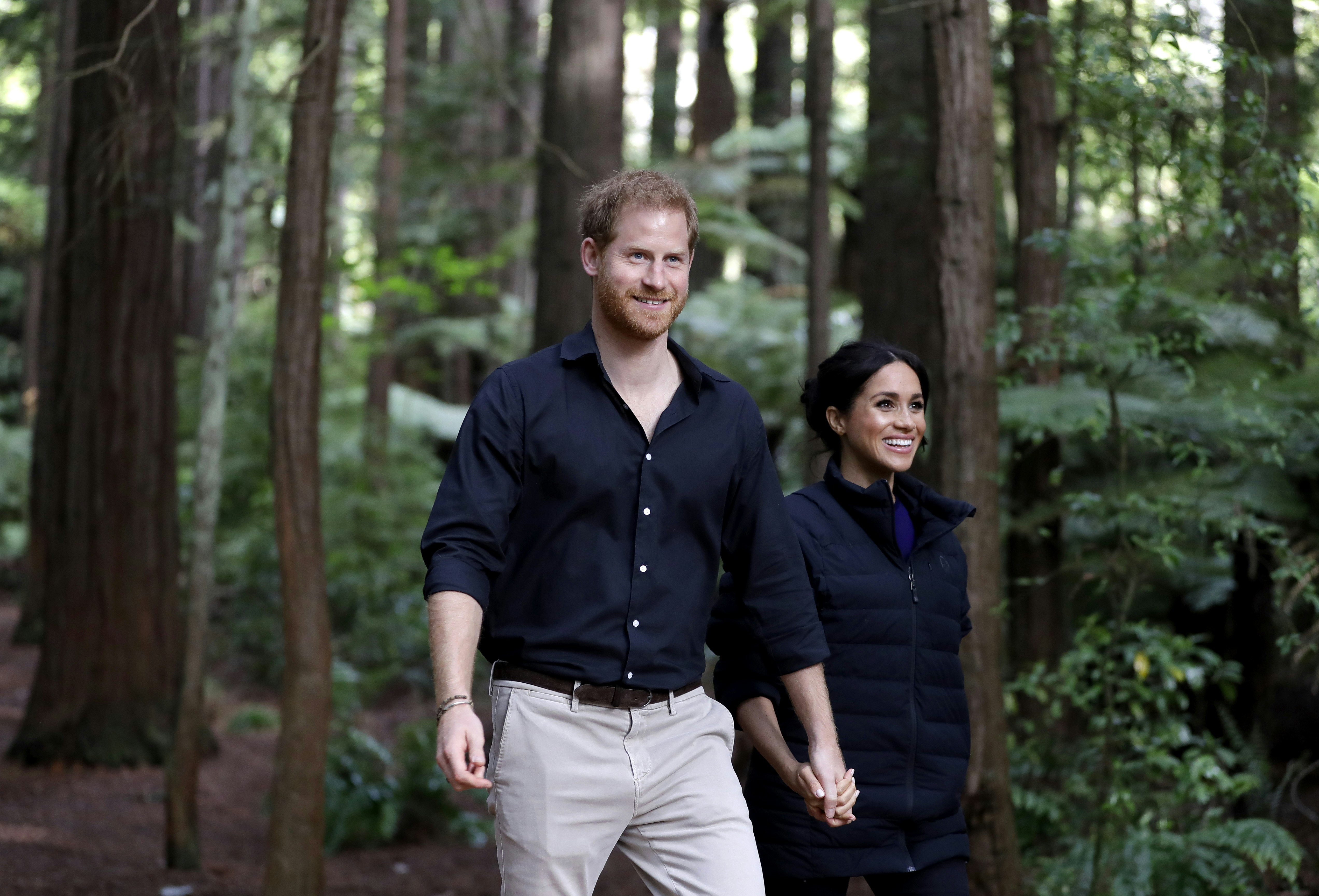 Prince Harry and Meghan Markle walk hand-in-hand in a redwood forest.