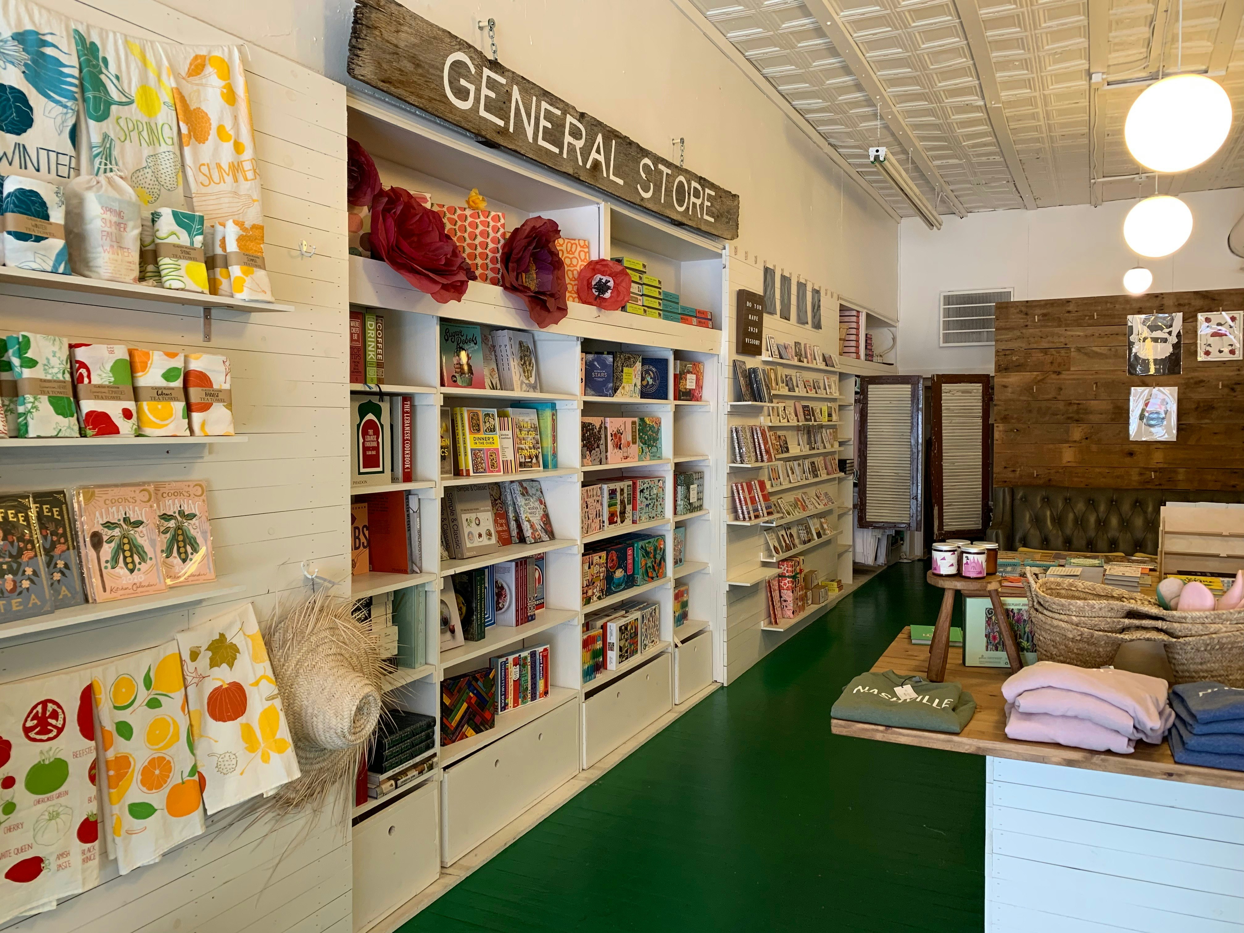 Interiören i Hey Rooster General Store visar färgglada kökshanddukar, böcker, t-shirts, pappersblommor, ljus och mer