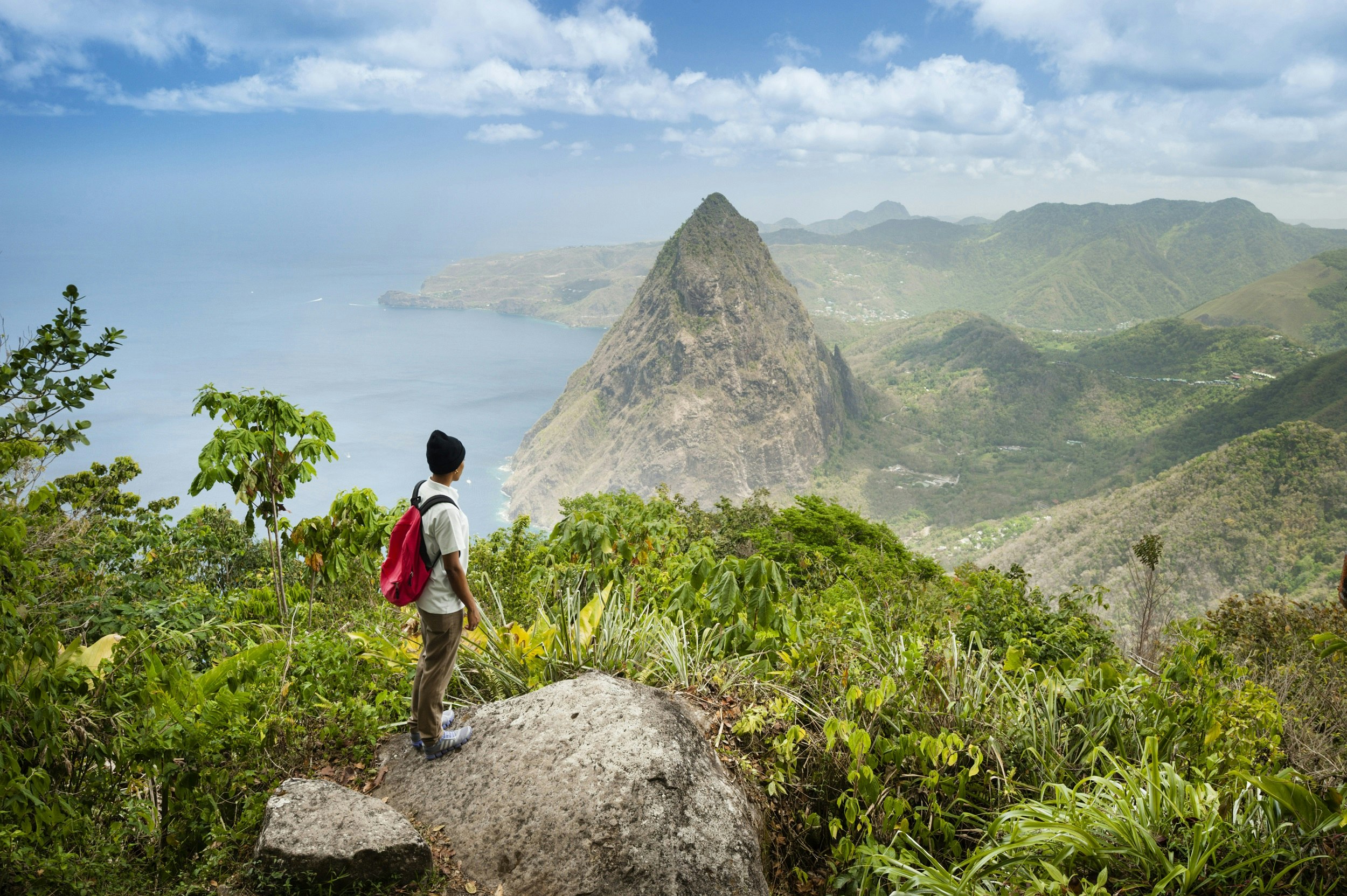 A hiker standing at lofty lookout overlooking Gros Piton in the distance; the coast is also seen far below.