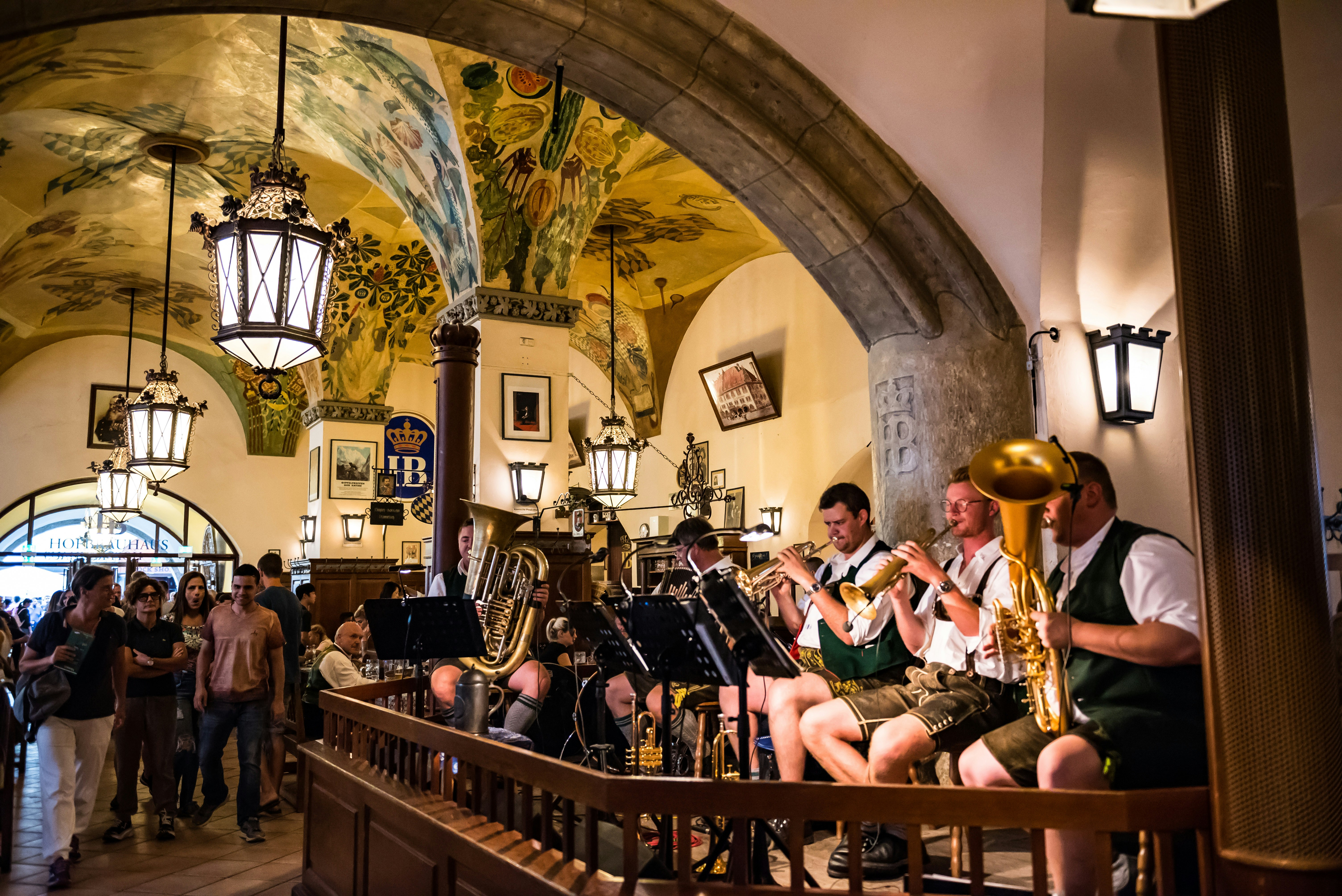 Inside Munich's famous Hofbräuhaus; the buttermilk yellow ceilings are painter with a floral design, and a group of people are watching a live brass band.