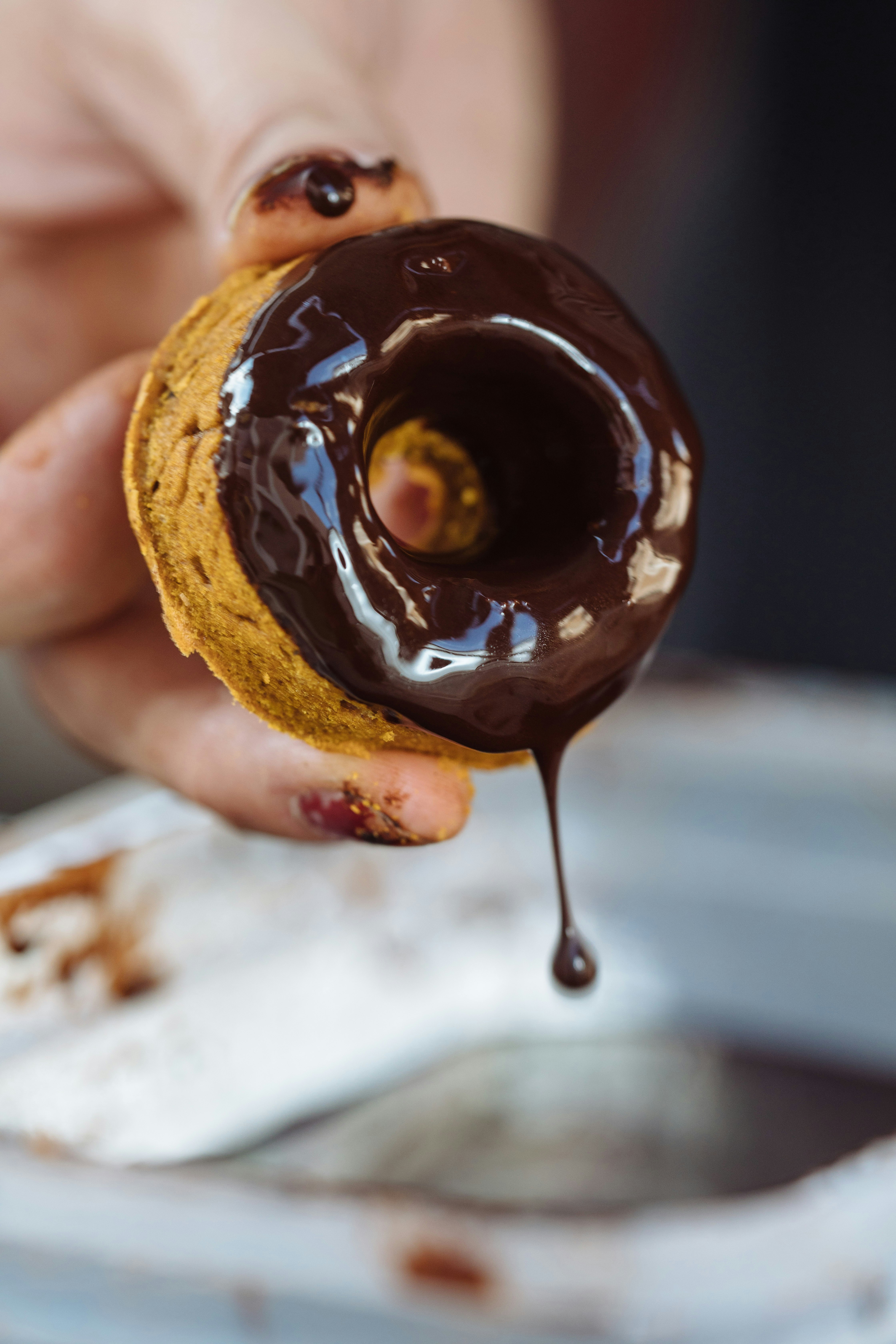 A close-up of a person holding a small, donut-shaped dog treat that has just been dipped in dog-friendly melted chocolate.