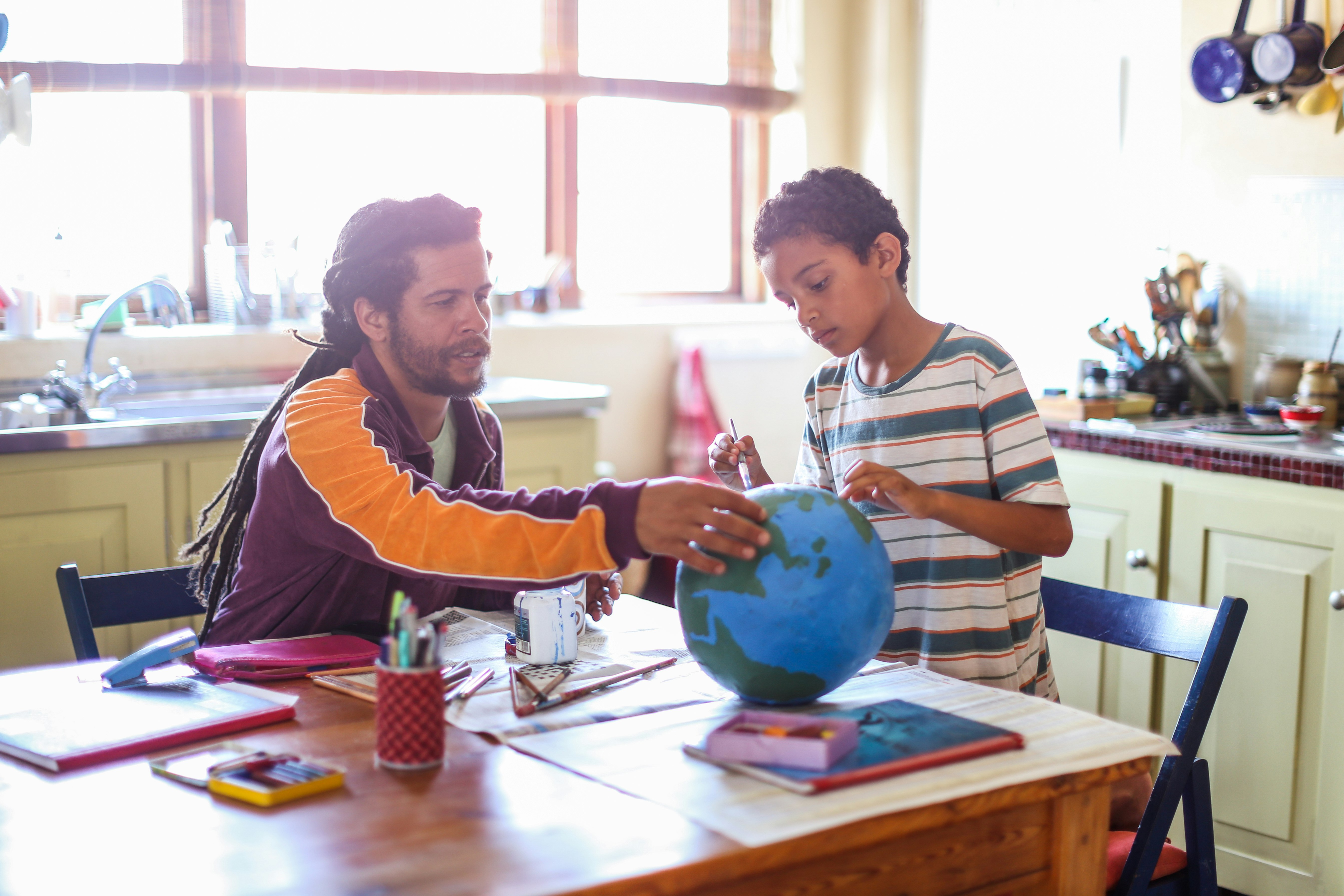 A man helps a boy with a paper mache globe