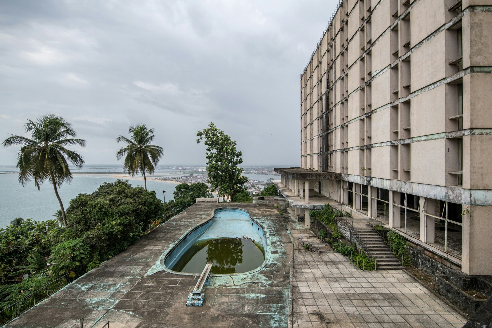 The overgrown remains of the Hotel Ducor stand atop a hill that looks over the ocean the Monrovia; the concrete tile deck features an algae filled swimming pool