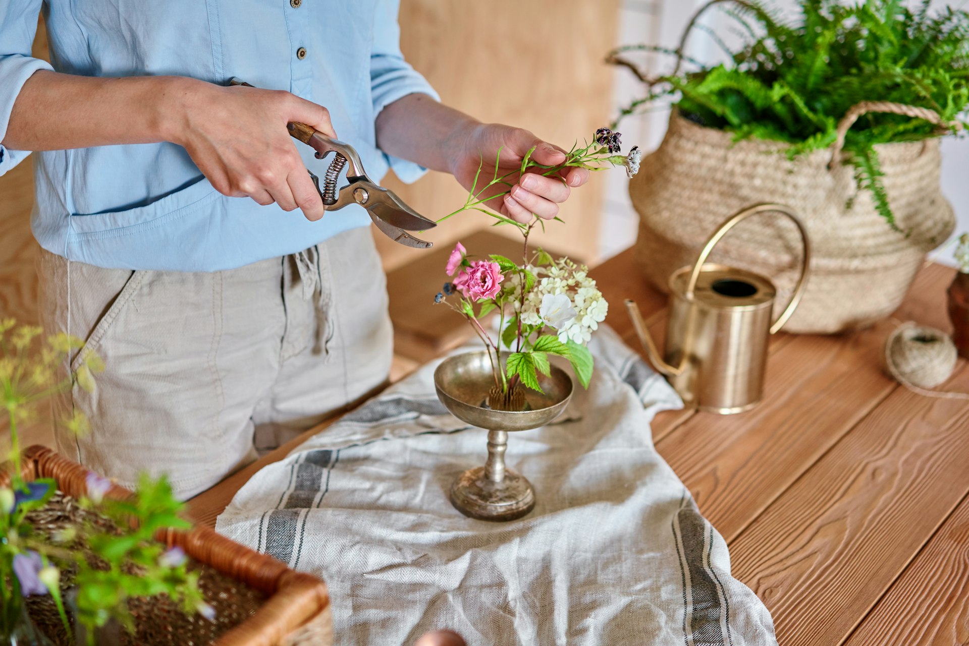 A person is using secateurs to trim the stem of a flower; their arranging flowers in the Japanese ikebana style.