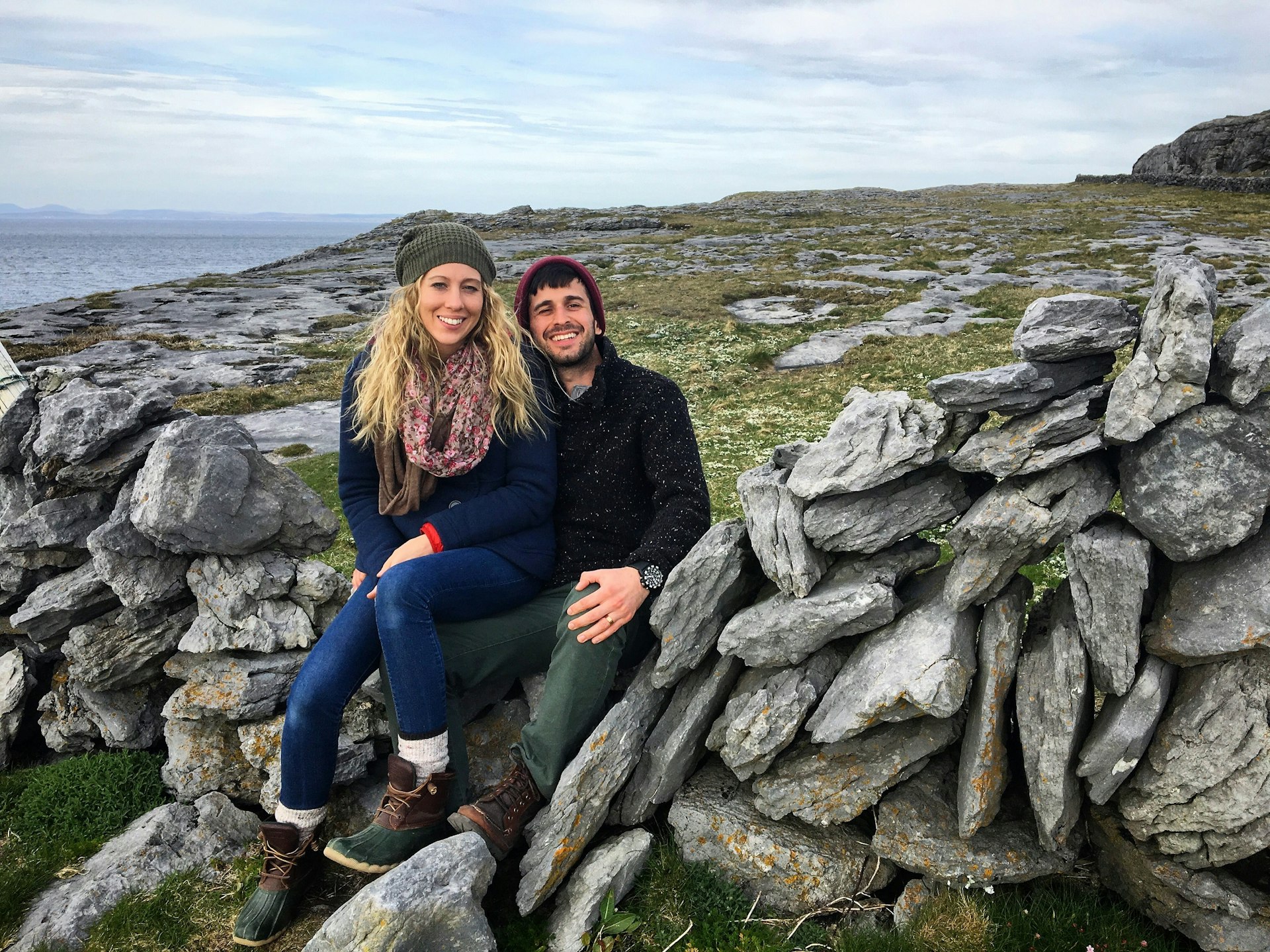 A couple in hiking gear sit on a stone wall in the Irish countryside