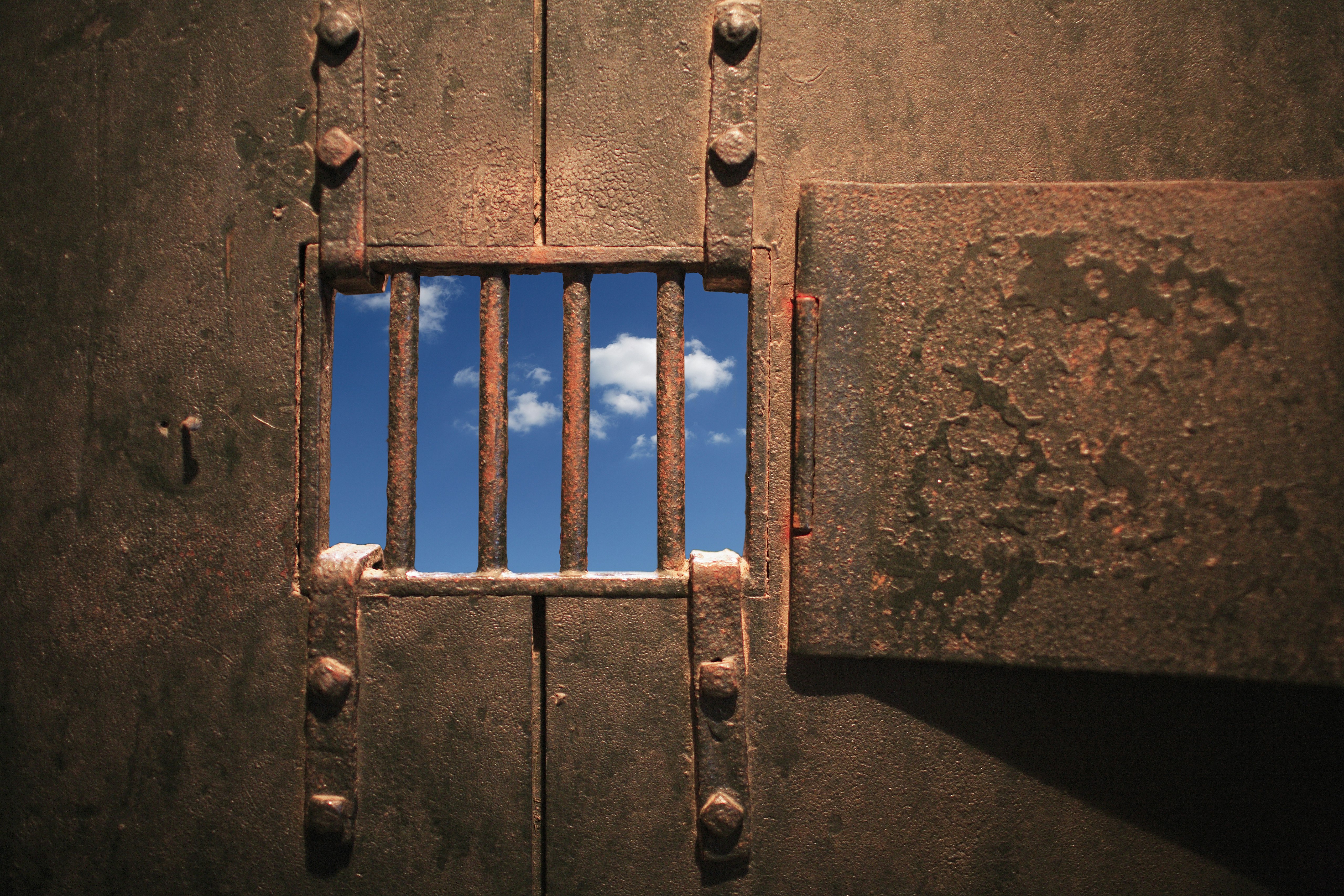 A clear blue sky is visible through the rusty bars of a prison door