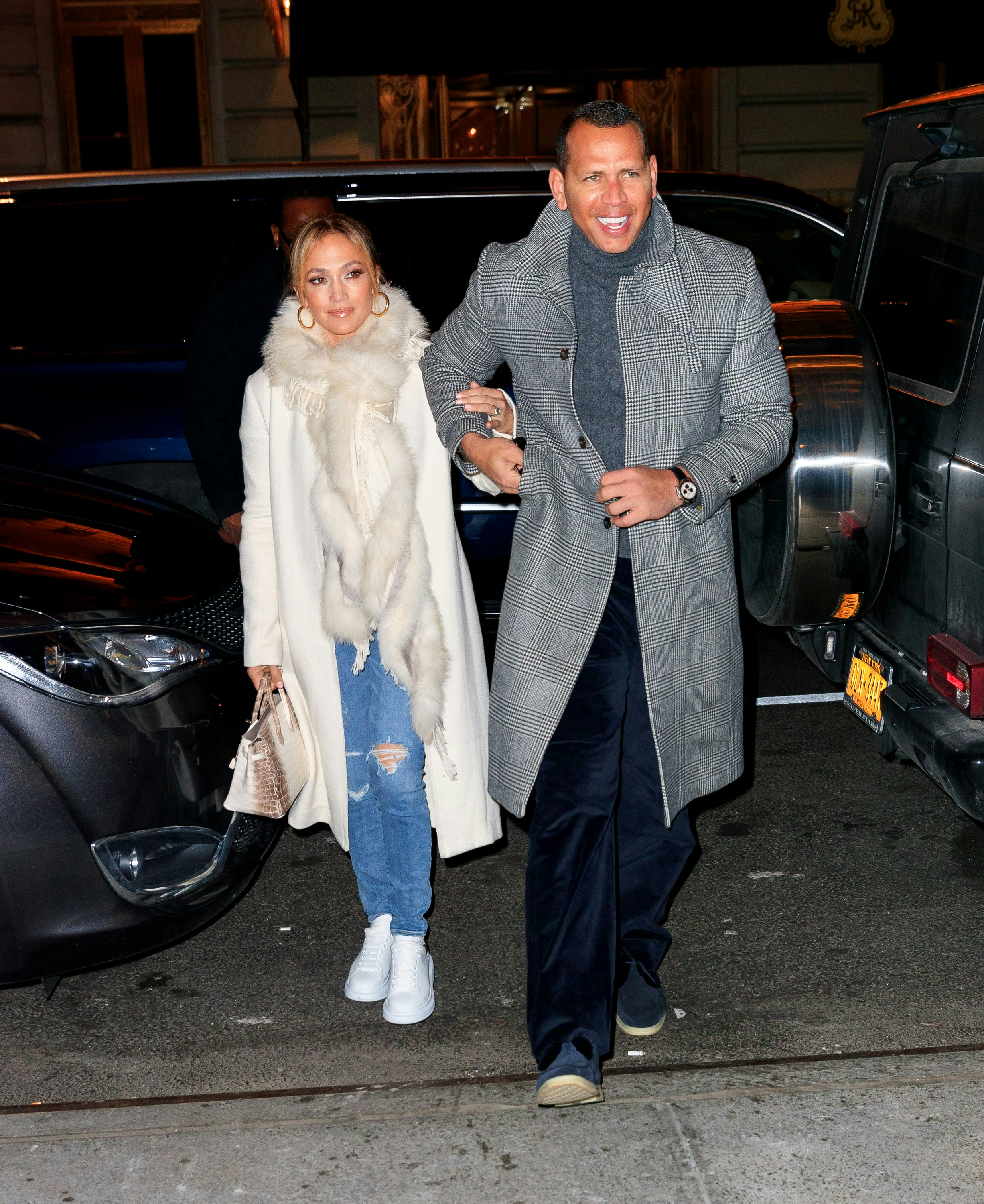 Jennifer Lopez and Alex Rodriguez walk arm-in-arm between parked cars.