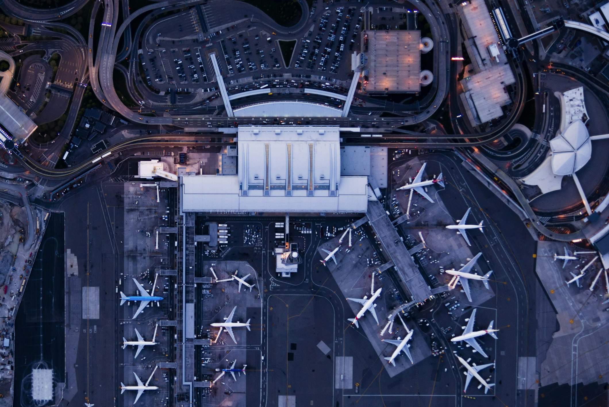 An aerial view in deep blue and dusty lavender tones of JFK airport in New York at night, with the white terminal in the upper center and white airplanes parked on the ground all around.jpg