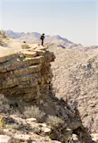 A trekker stands on the edge of a cliff and overlooks a dramatic rocky canyon.